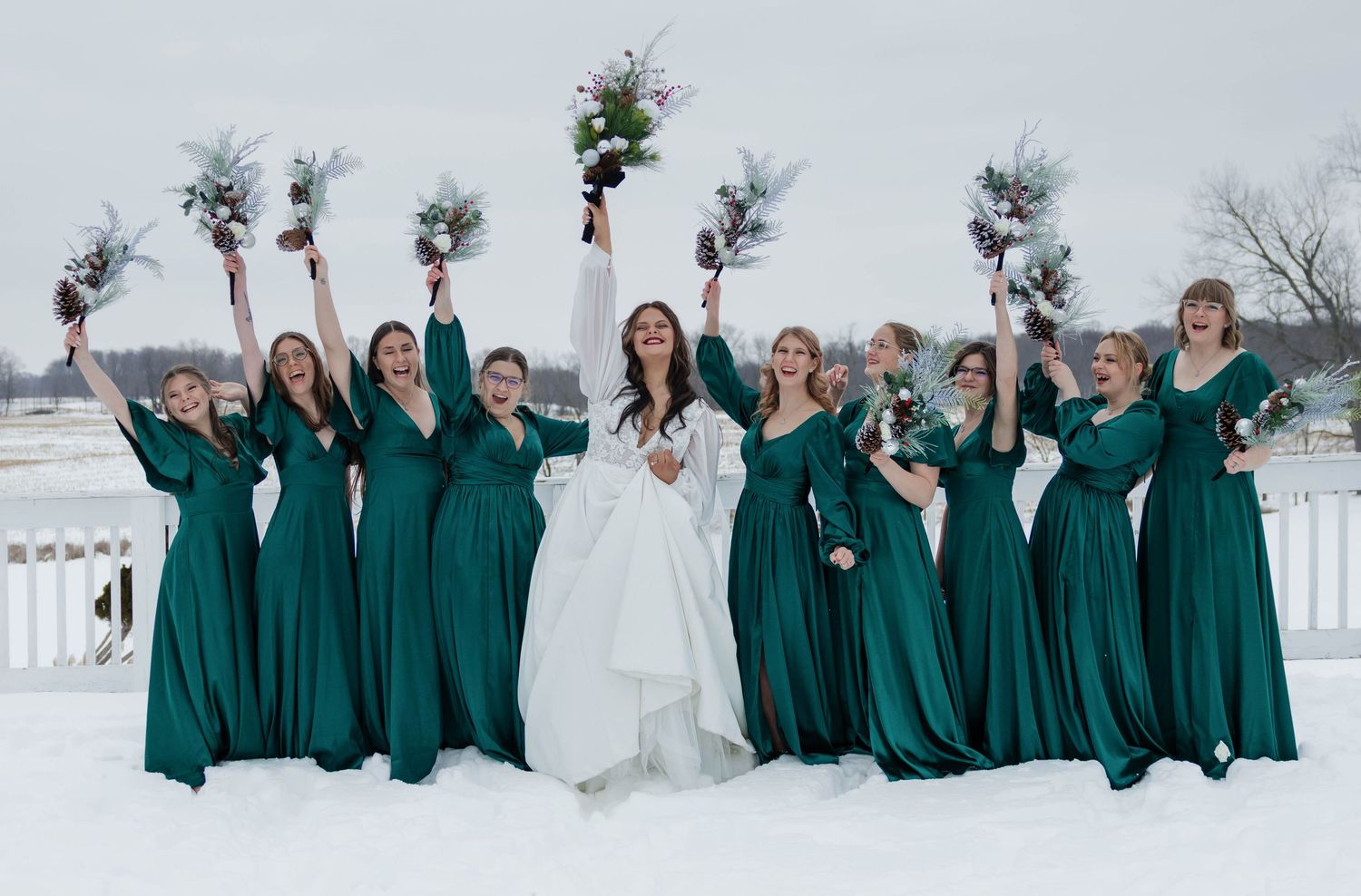 Bride with bridesmaids in emerald green dresses celebrating outdoors in snowy winter wedding setting.