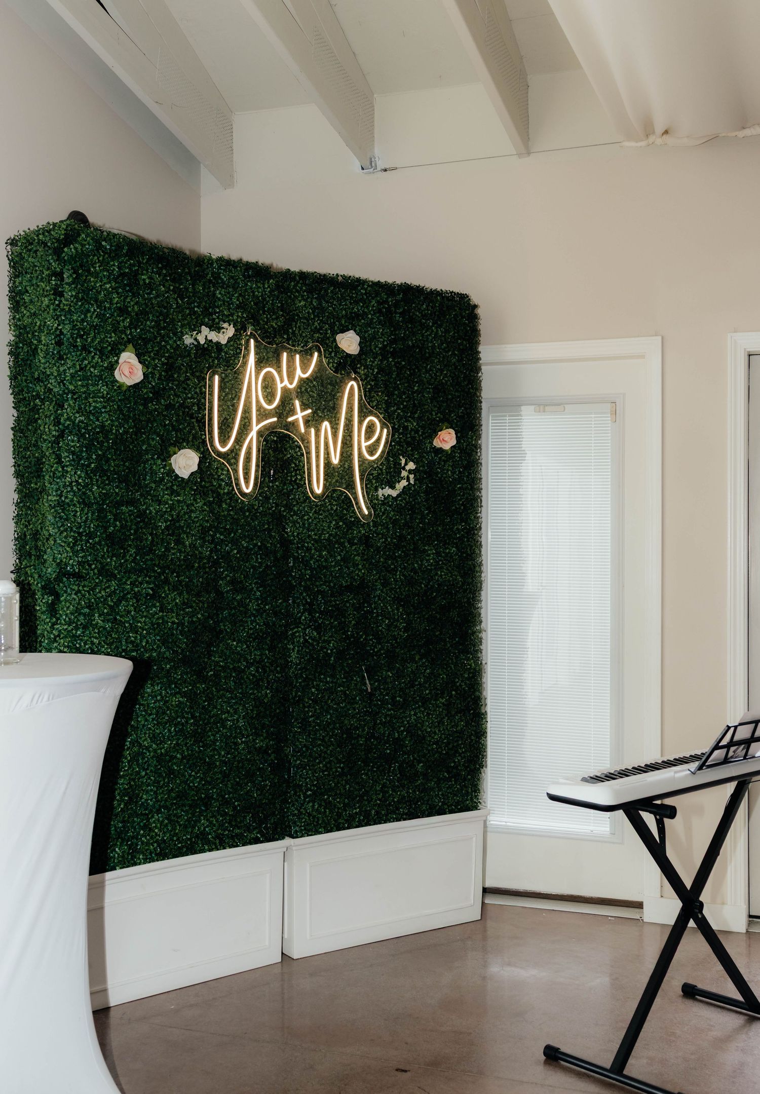 Green hedge wall with glowing You and Me neon sign at a wedding reception venue.