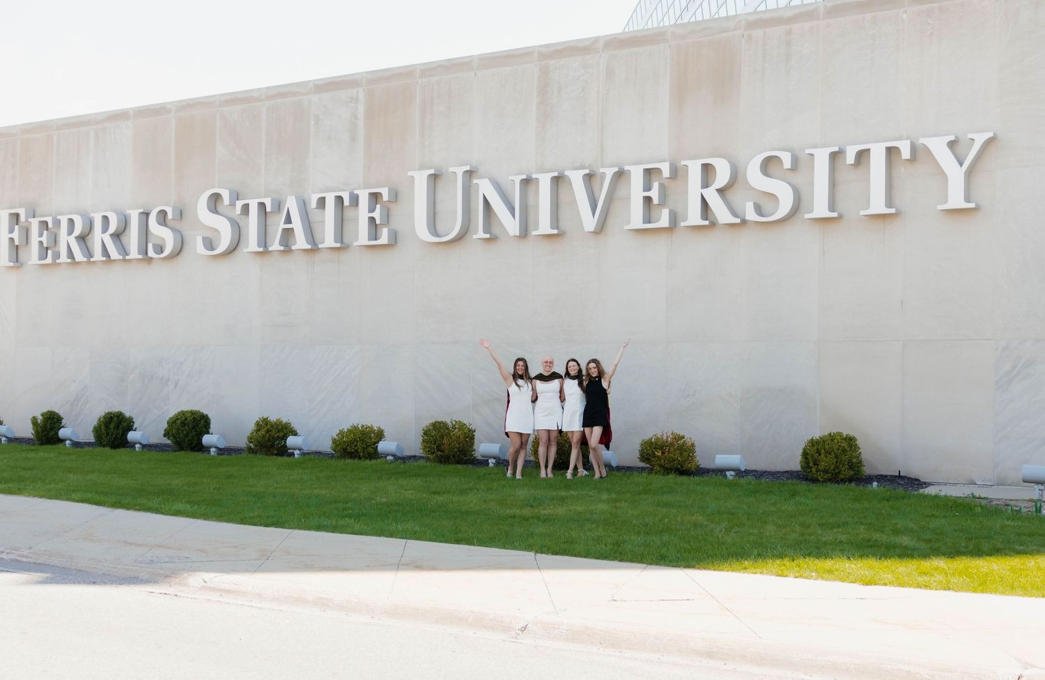 Four young women posing together in front of Ferris State University sign at dusk.