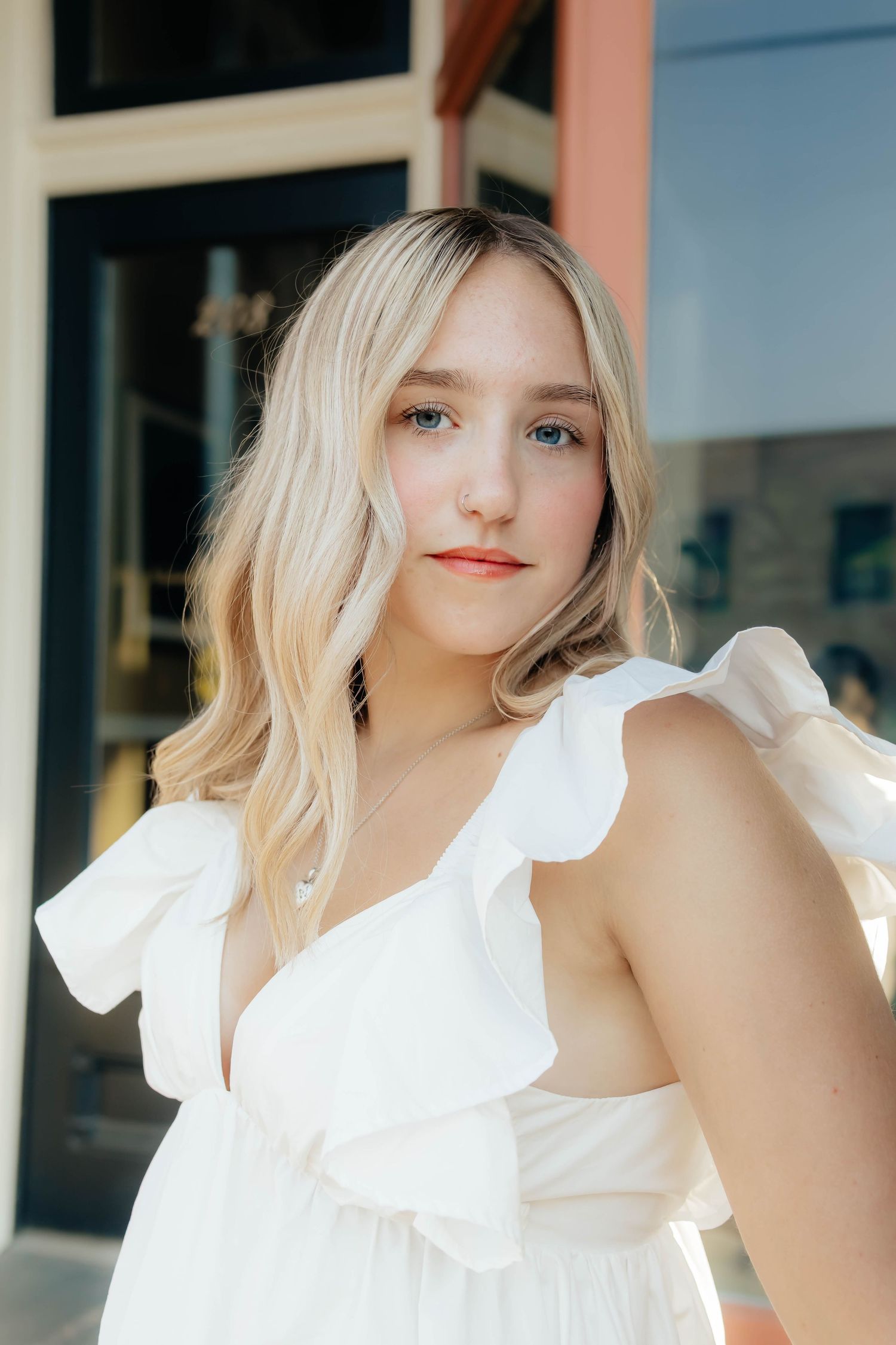 Young blonde woman in white ruffle dress posing outdoors for senior portrait photography.