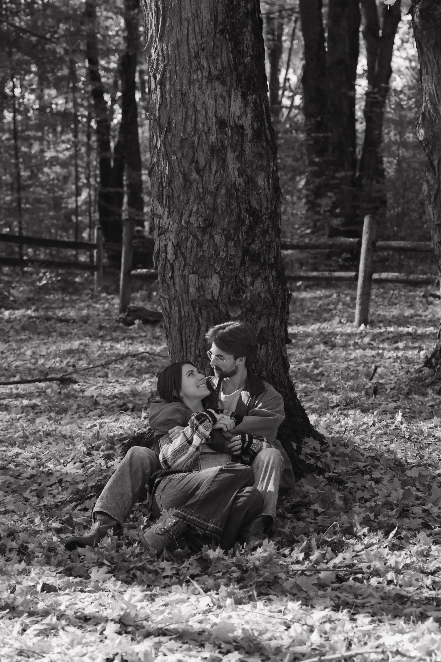 Romantic black and white photo of a couple about to kiss beside a tree in autumn woods.