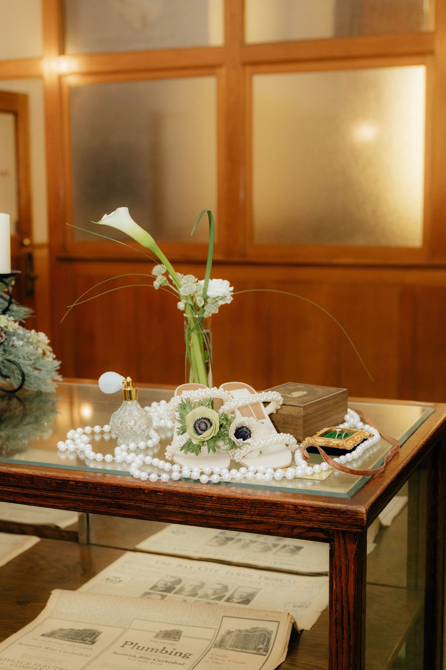 Vintage wedding display table with calla lily vase, pearl necklace, and antique decorative items.