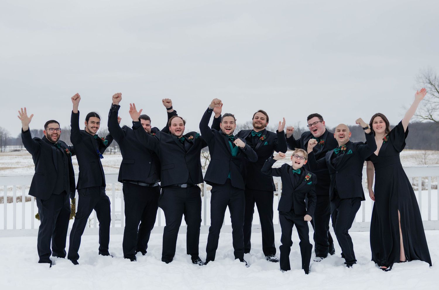 Groomsmen and wedding party celebrating with raised arms in snowy outdoor winter wedding photo.