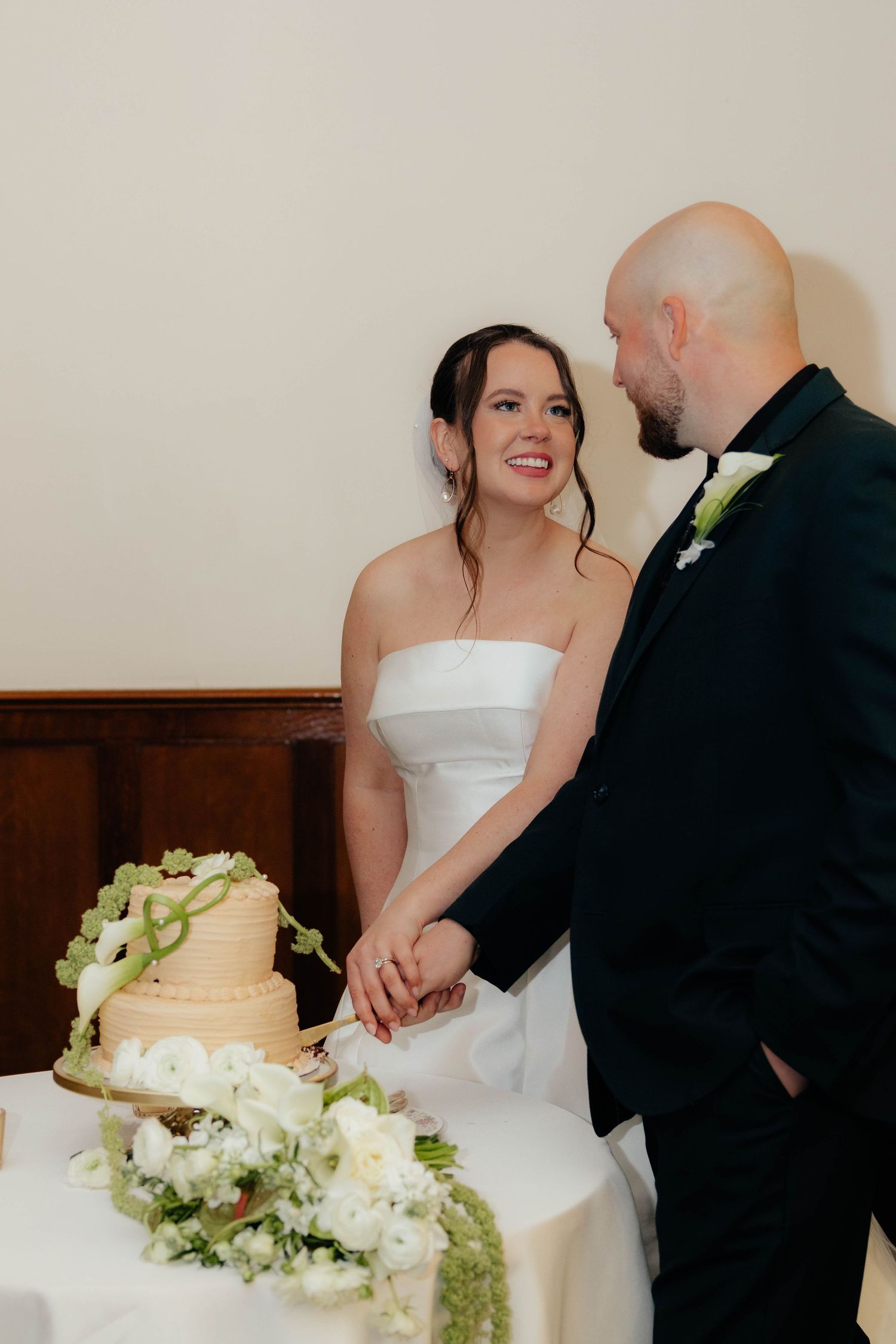 Smiling bride and groom cut wedding cake together at reception table.