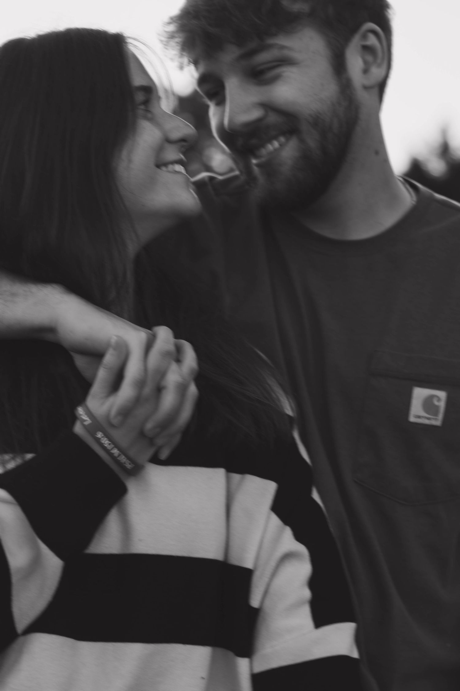 Black and white close-up of a couple smiling and holding hands outdoors.