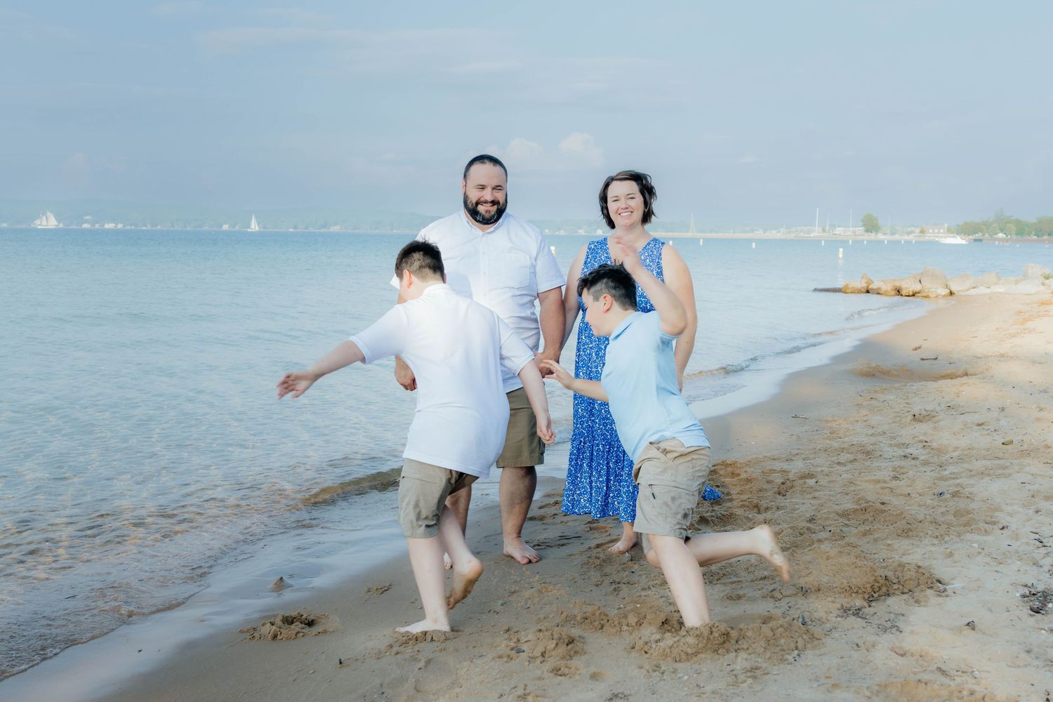 Family of four playing on a sandy beach shore with calm blue water in the background.