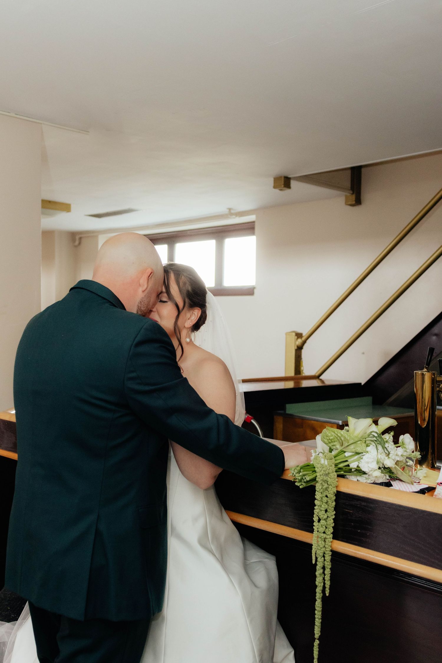 Bride and groom sharing an intimate moment beside a piano decorated with white floral arrangements.