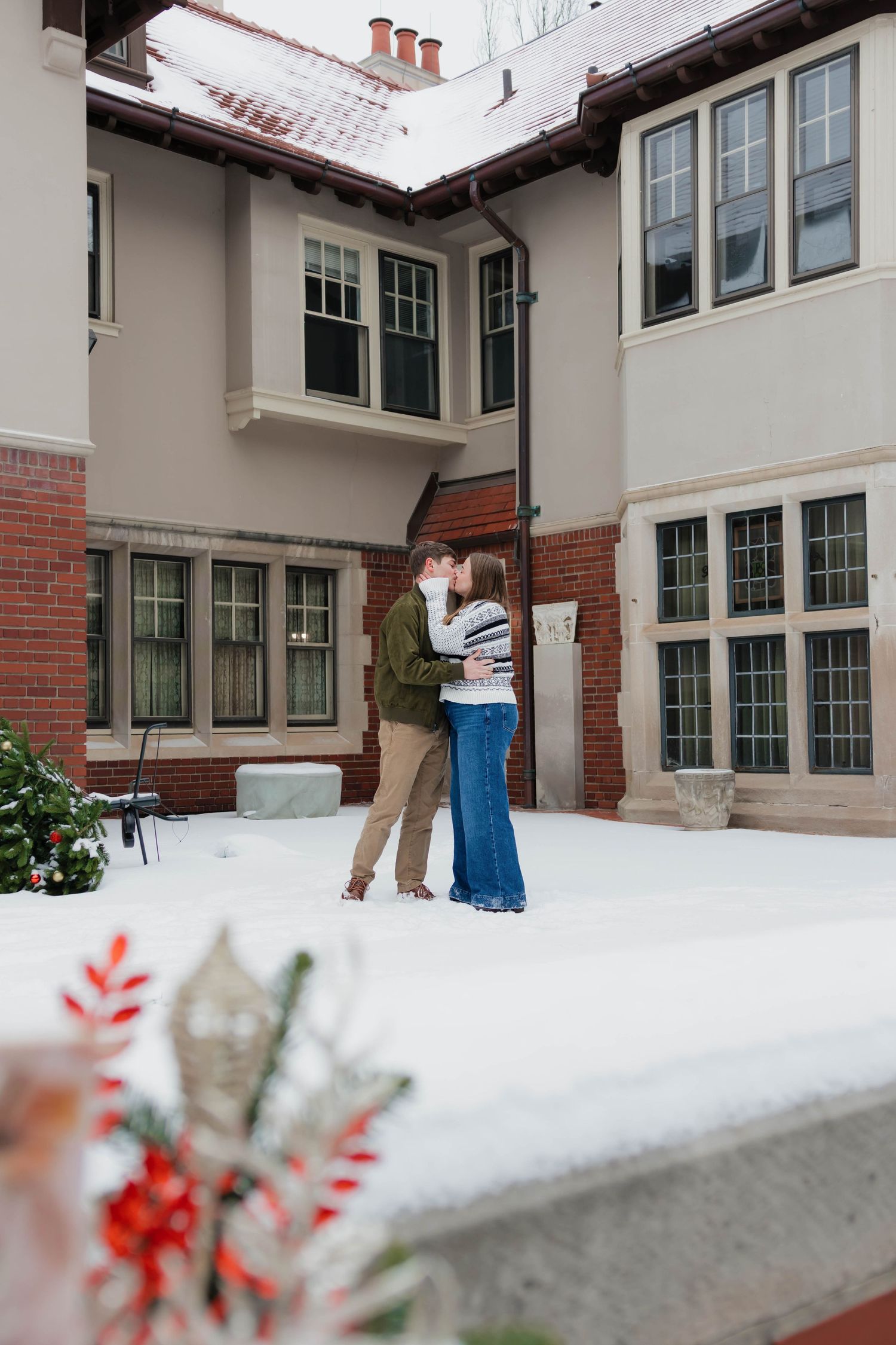 Couple sharing a kiss in a snowy courtyard surrounded by a classic brick and stone building.