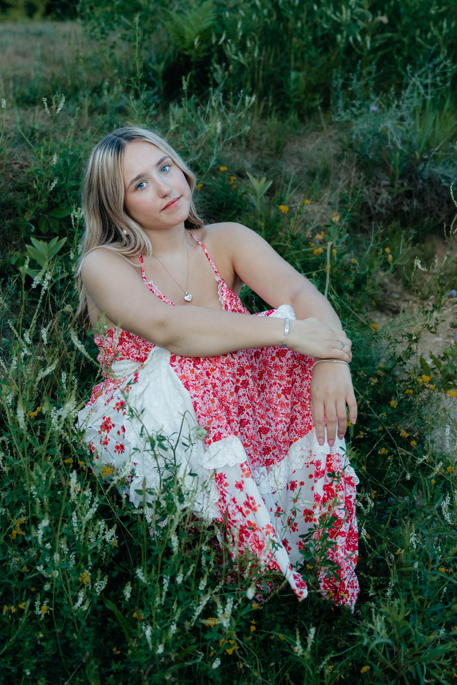 Blonde woman in red floral dress sitting in green meadow.