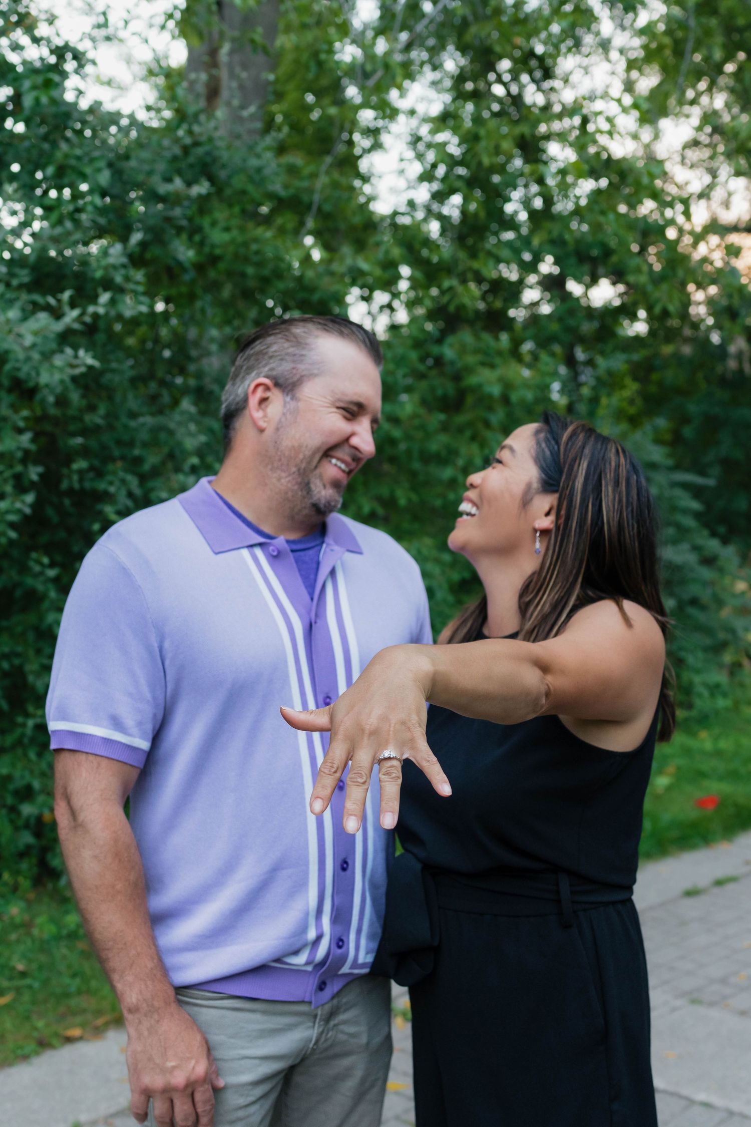 Laughing couple sharing a joyful moment while showing off an engagement ring.