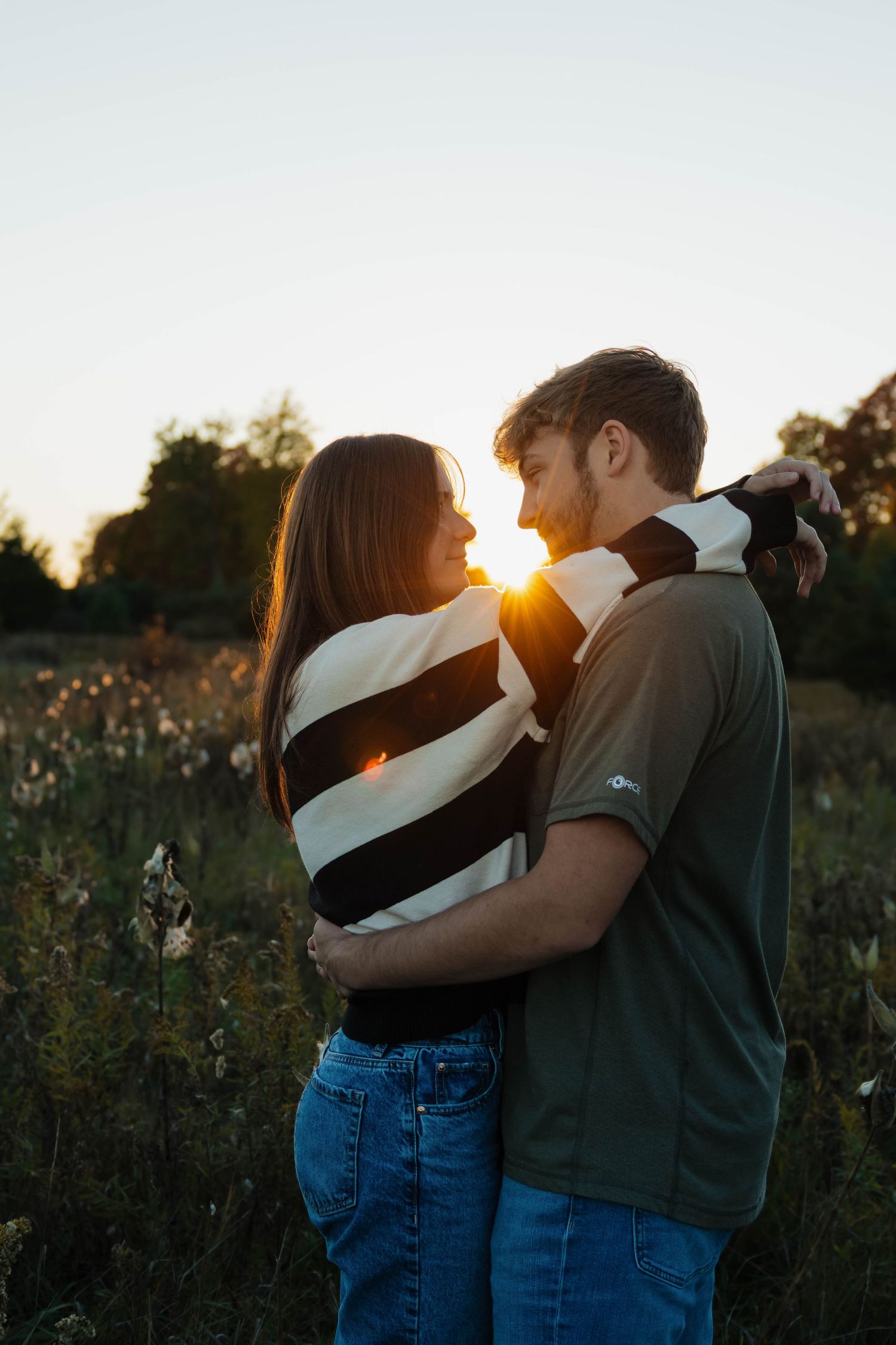 Couple embracing face to face in a wildflower field with a stunning golden sunset behind them.