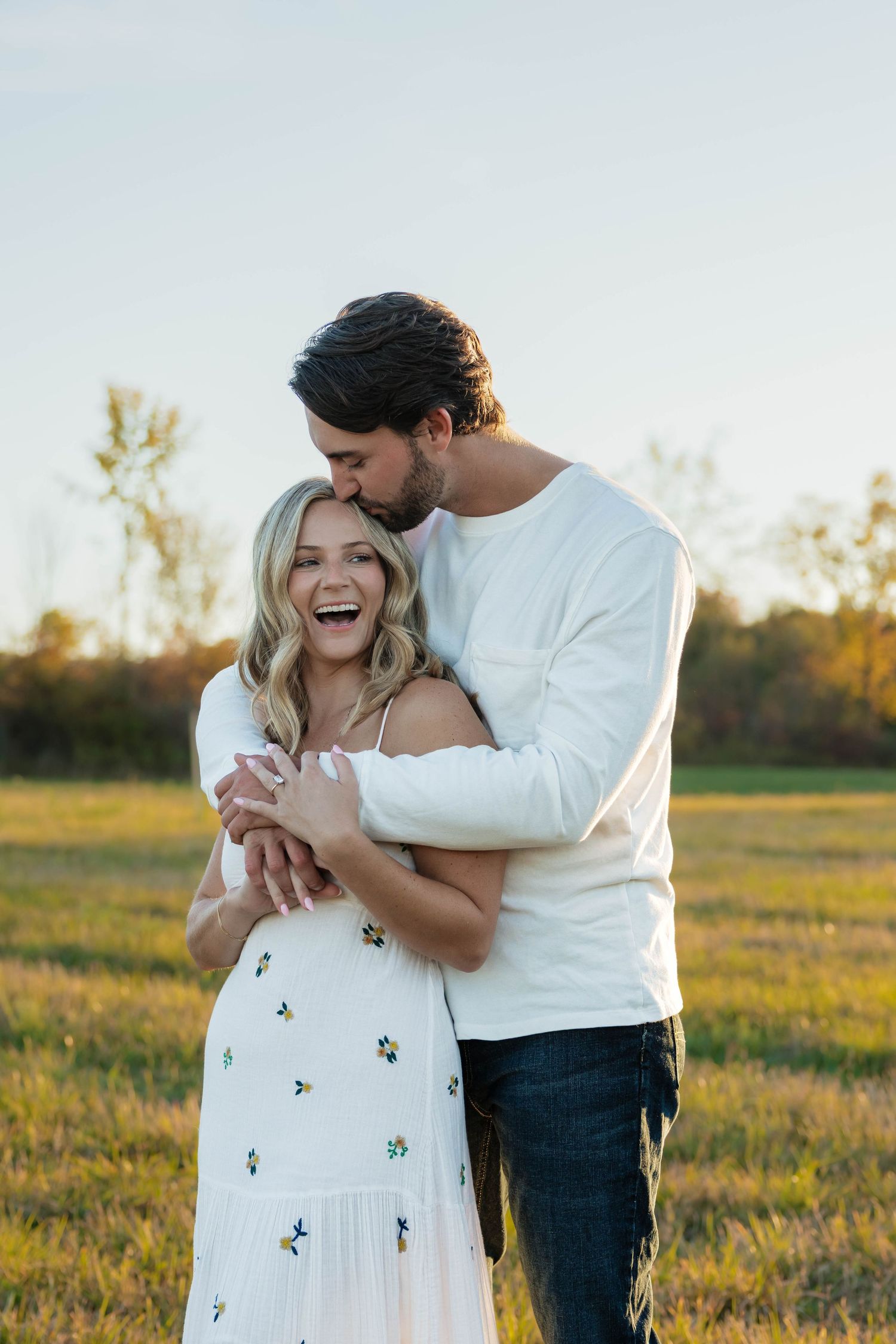 Man embracing and kissing a laughing woman in a floral dress in an open field.