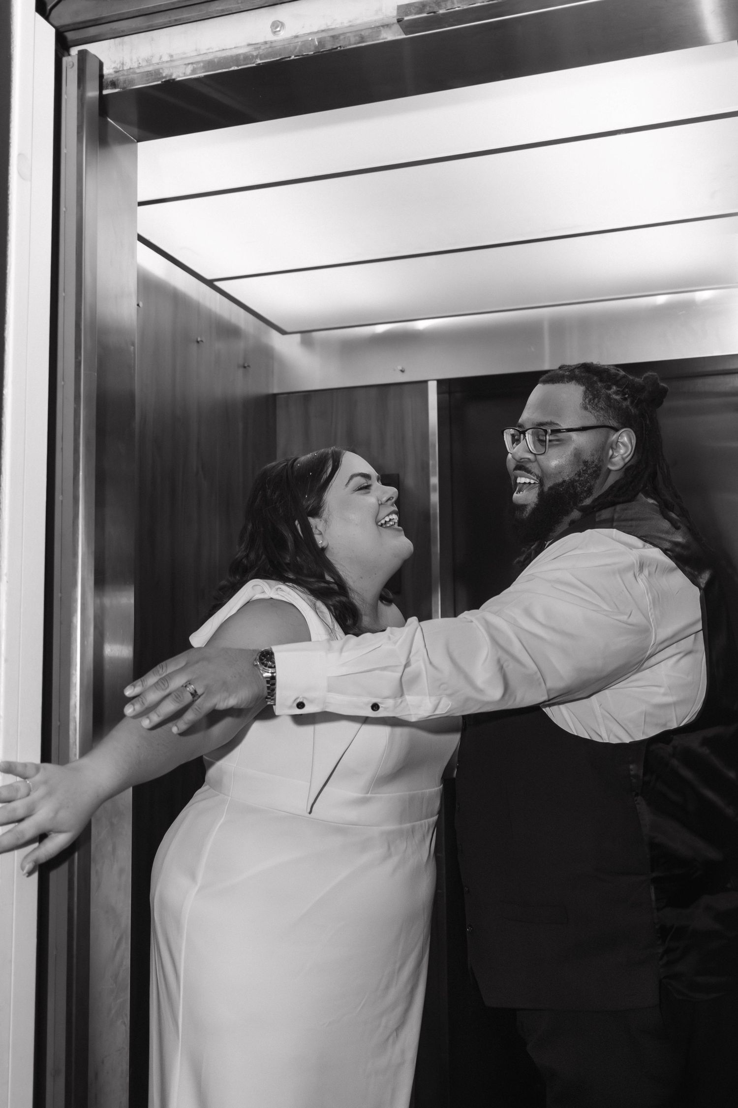 Black and white photo of laughing bride and groom embracing inside an elevator.