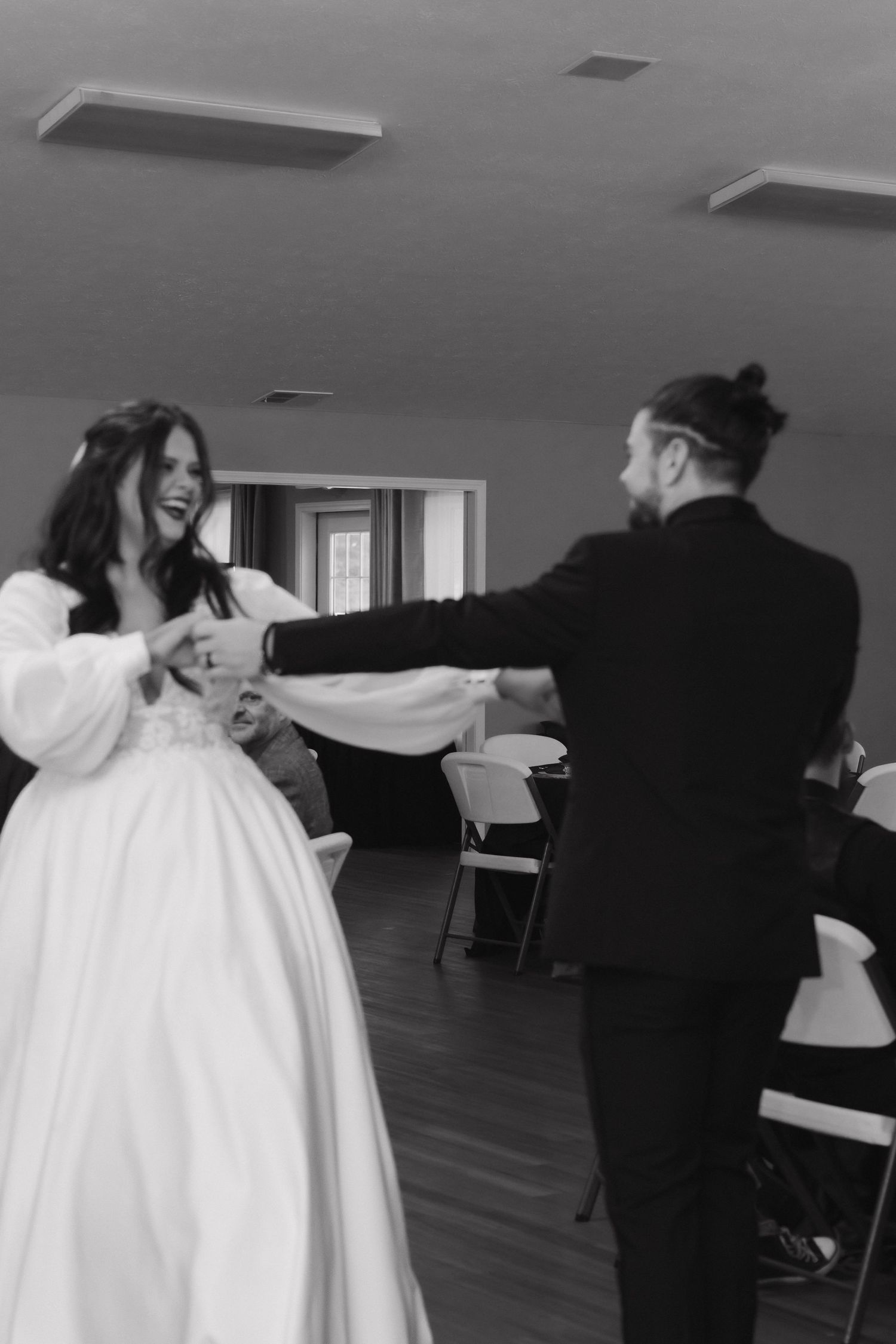 Bride and groom share joyful first dance in black and white photo at wedding reception.