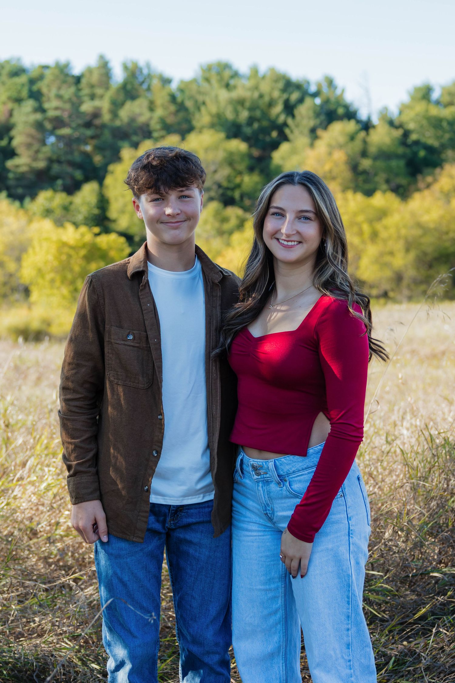 Smiling teenage boy and girl posing together in a sunlit autumn field.