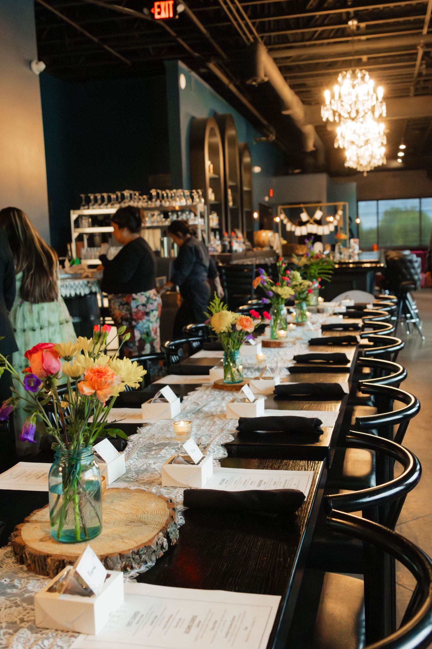 Long decorated reception table with colorful floral centerpieces on wood slices in a stylish restaurant venue.