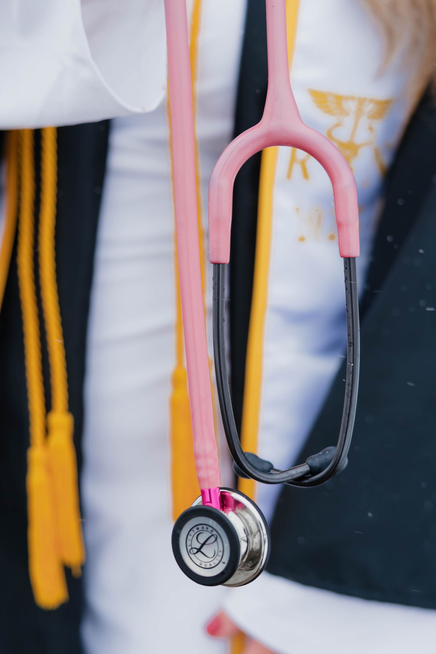 Close-up of a pink stethoscope draped over a nursing graduation gown with gold honor cords.