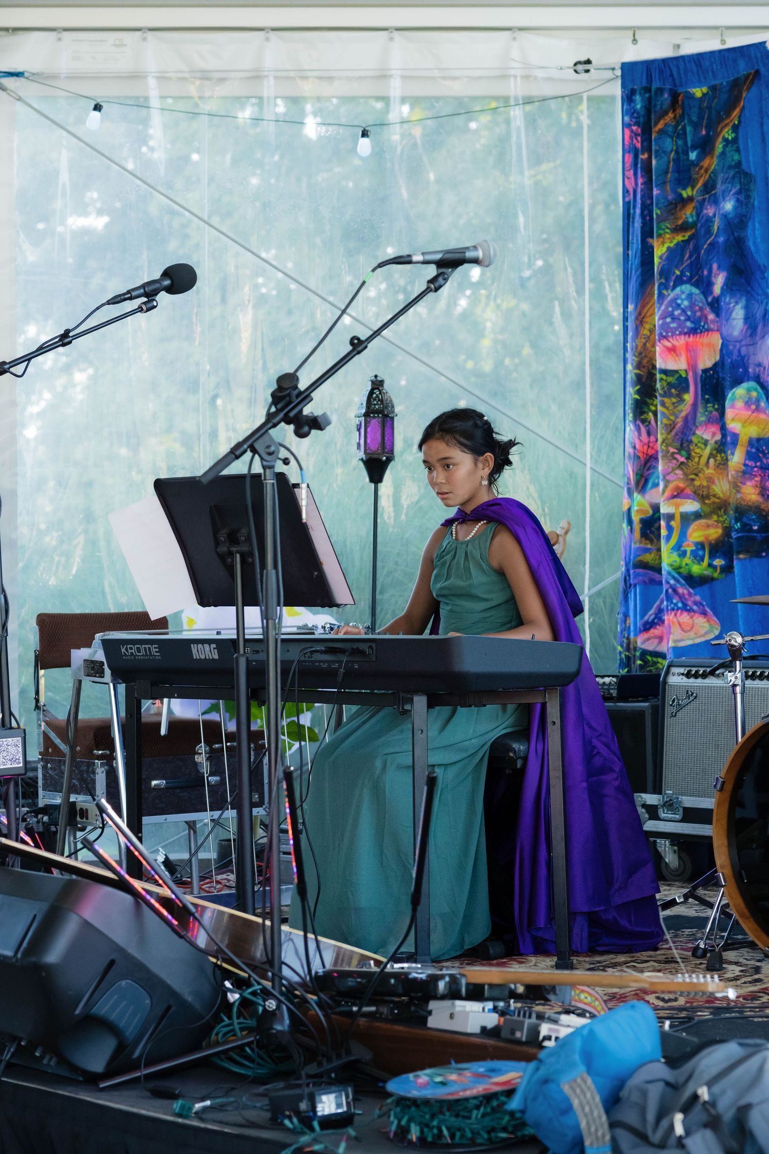 Young woman in teal and purple gown plays keyboard on stage at outdoor wedding reception tent.