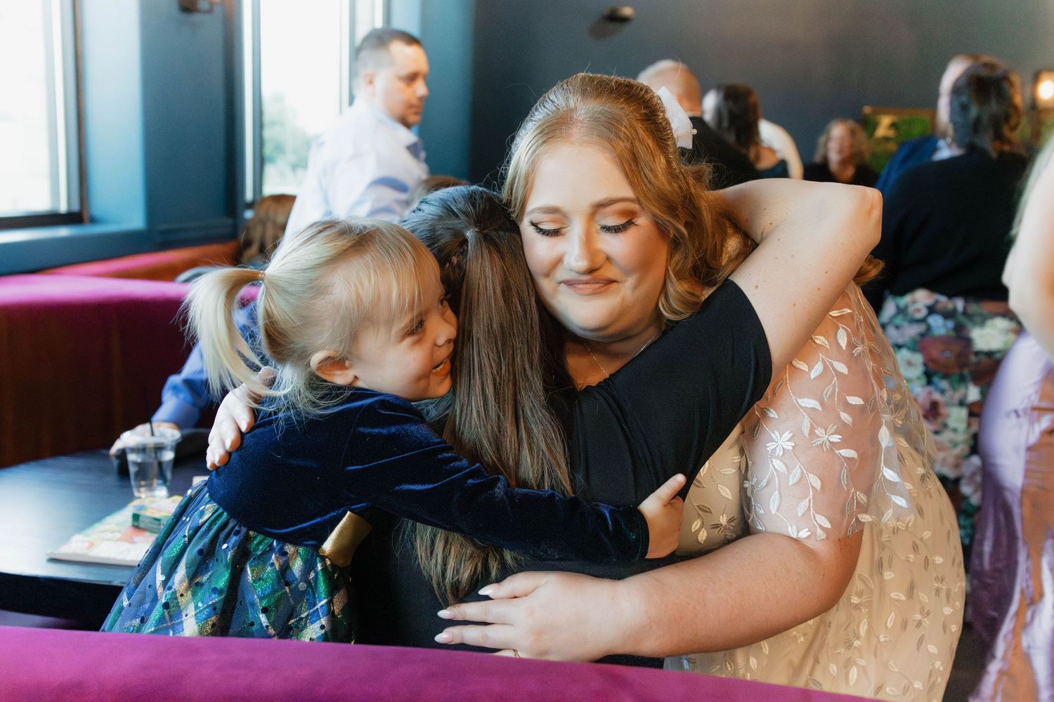 Bride in a sequined dress shares a warm hug with a young child at the reception.