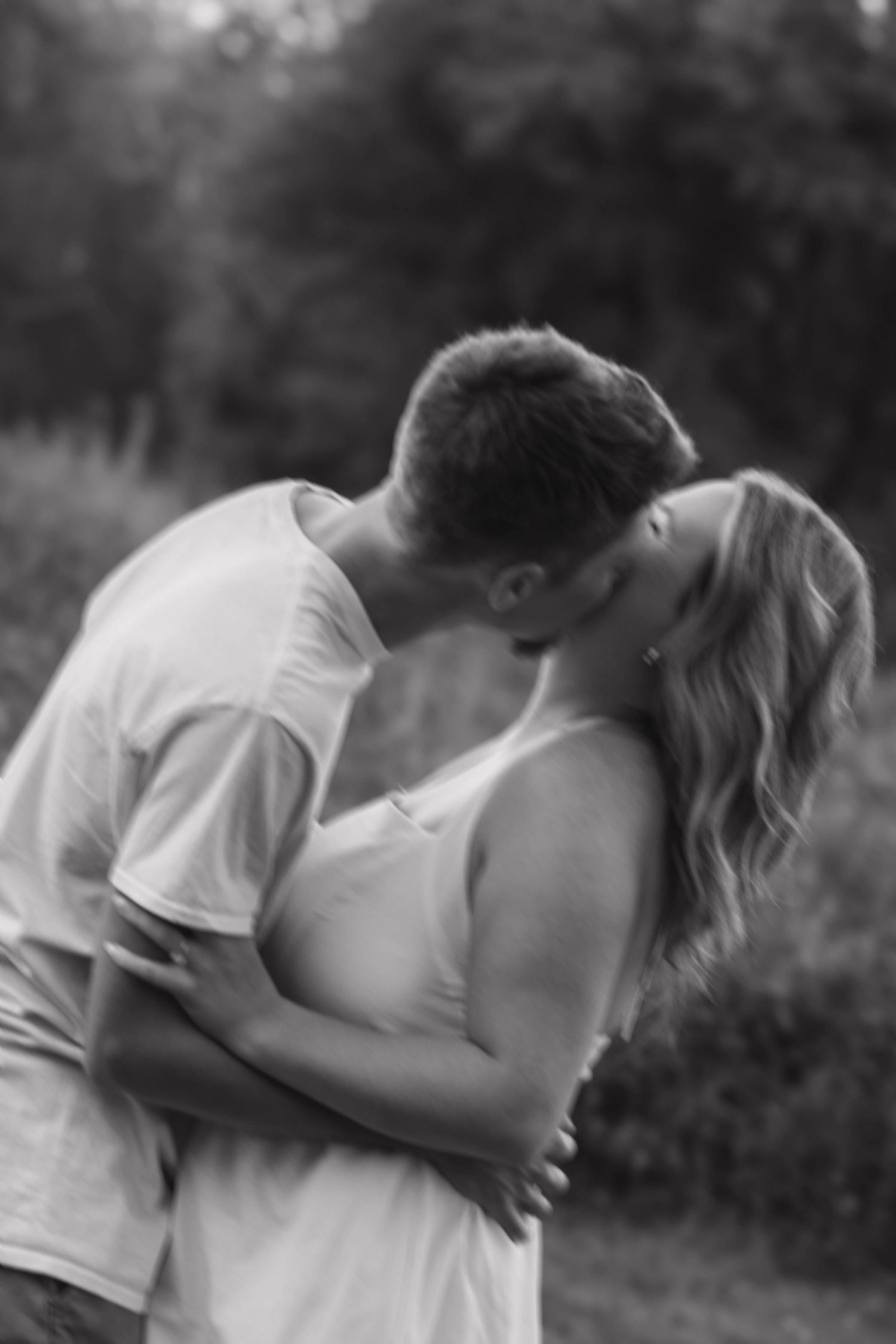 Black and white photo of a couple sharing a romantic kiss outdoors, embracing tenderly.