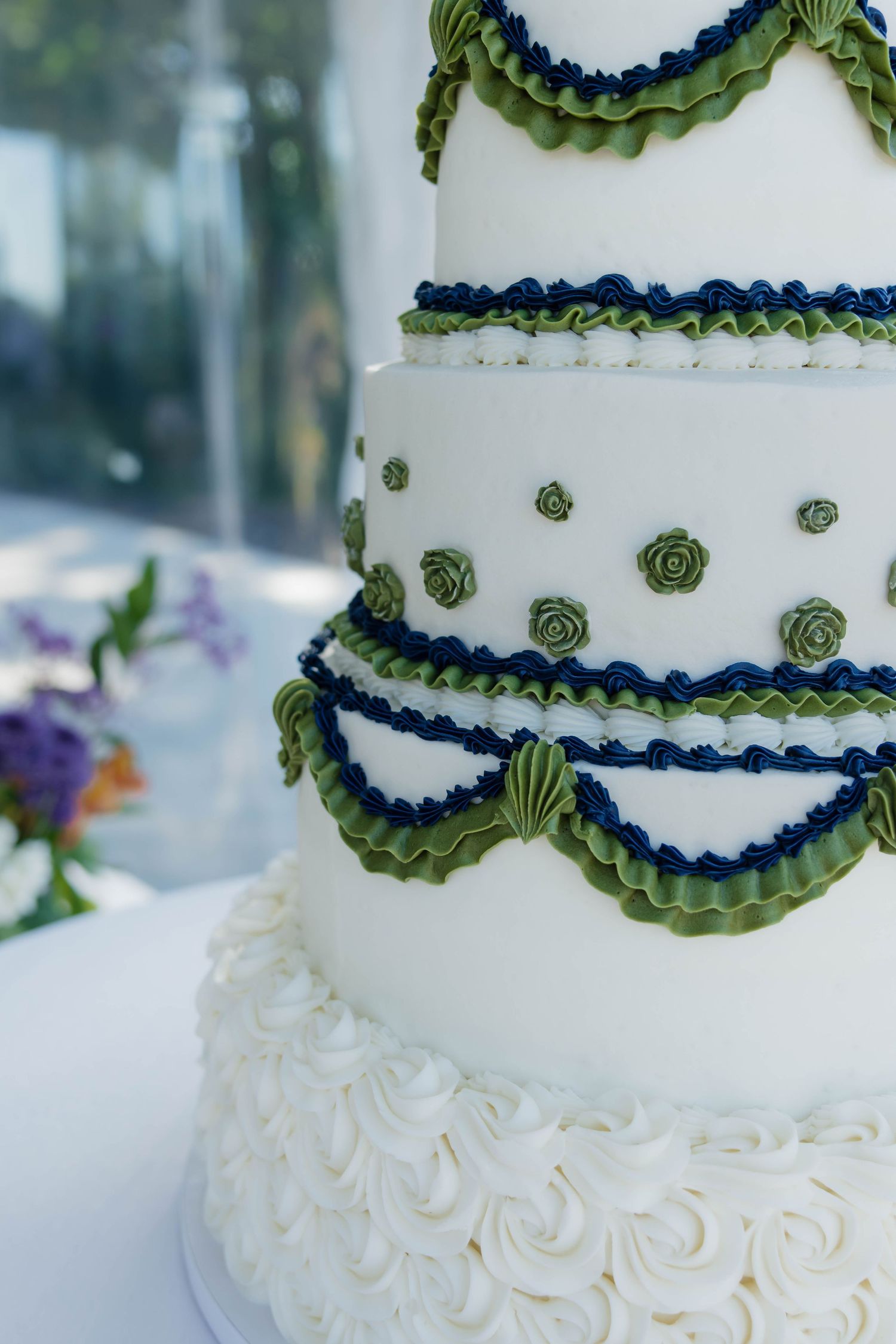 Close-up of elegant white wedding cake with green ruffled swags, navy trim, and rosette base.