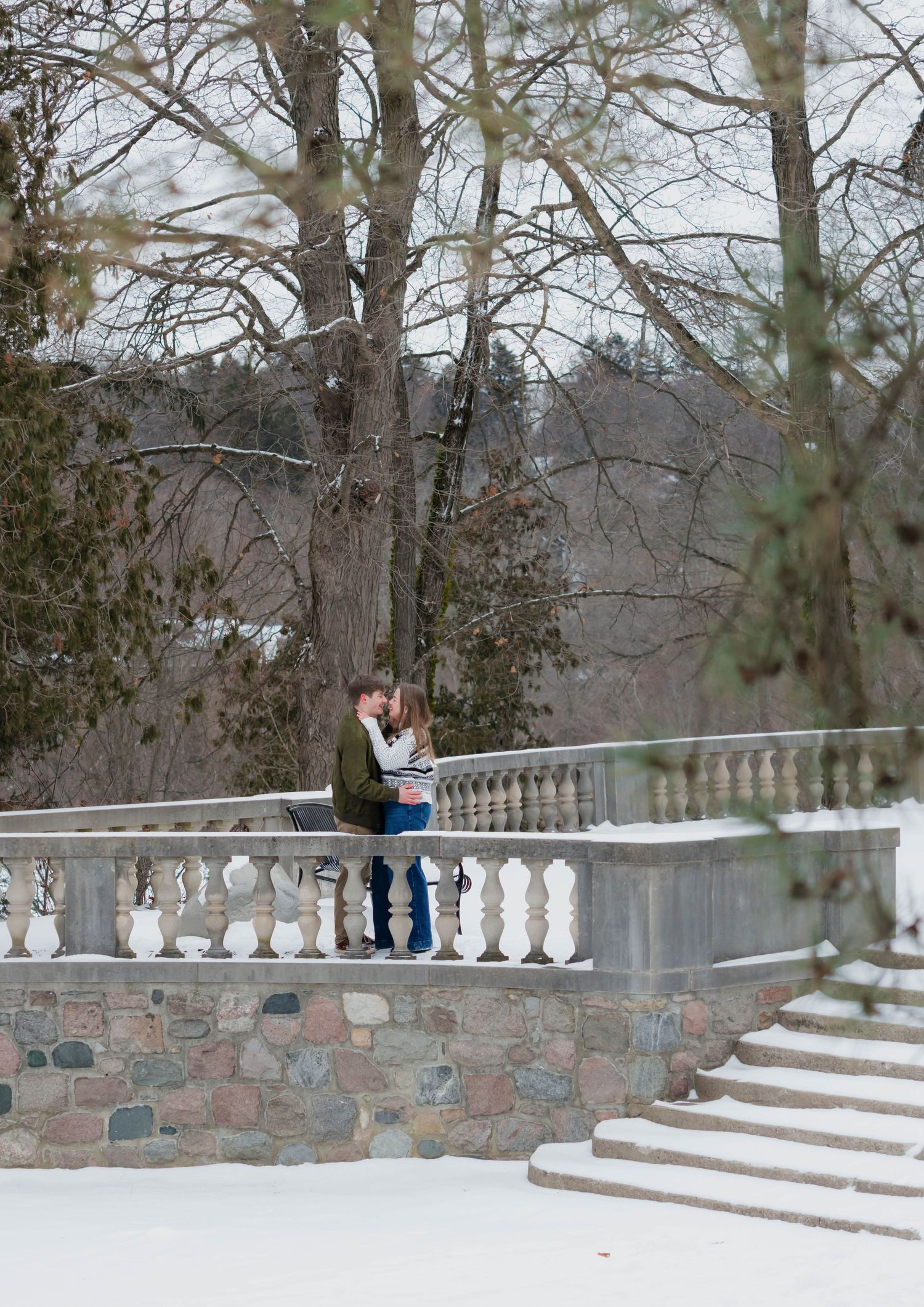 Couple kissing on a stone balustrade terrace surrounded by snow-covered winter landscape.