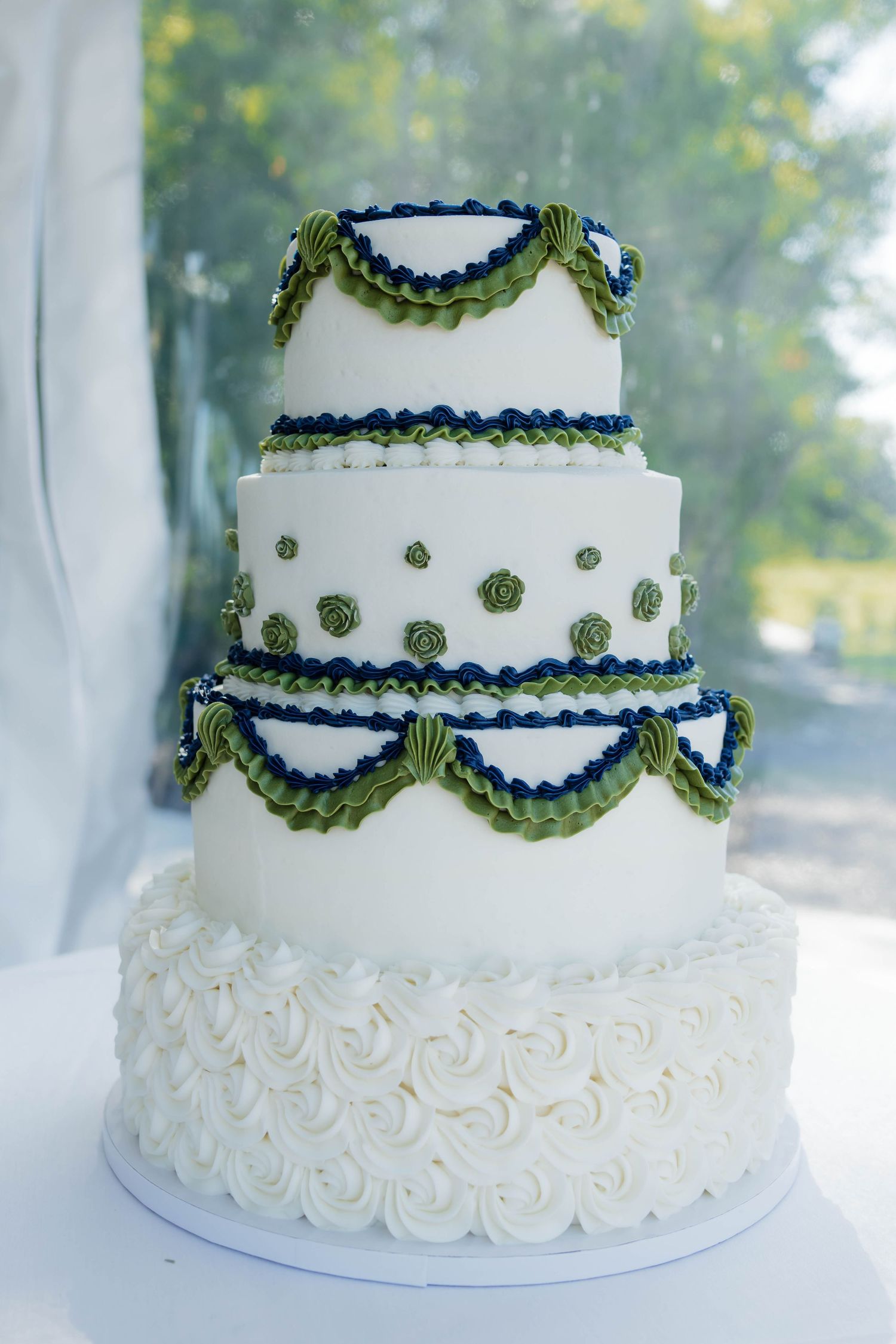 Three-tier white wedding cake adorned with green garland swags and navy blue piping details.