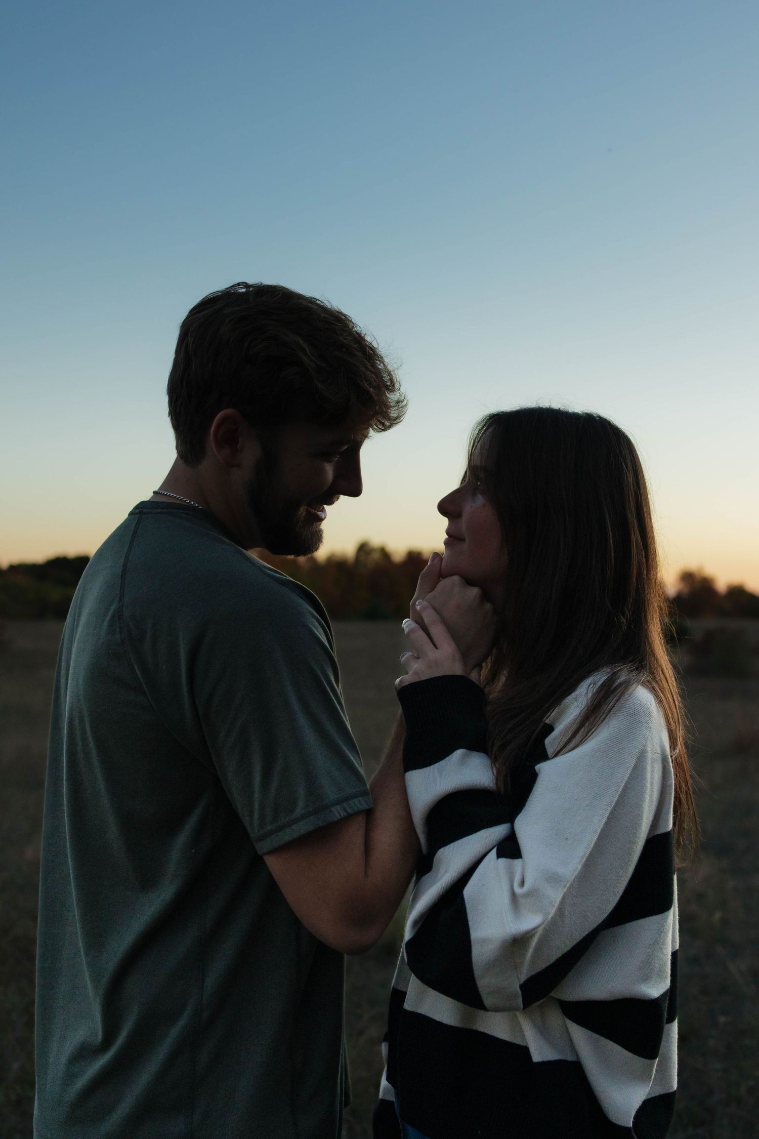 Couple facing each other holding hands during a golden sunset outdoors.