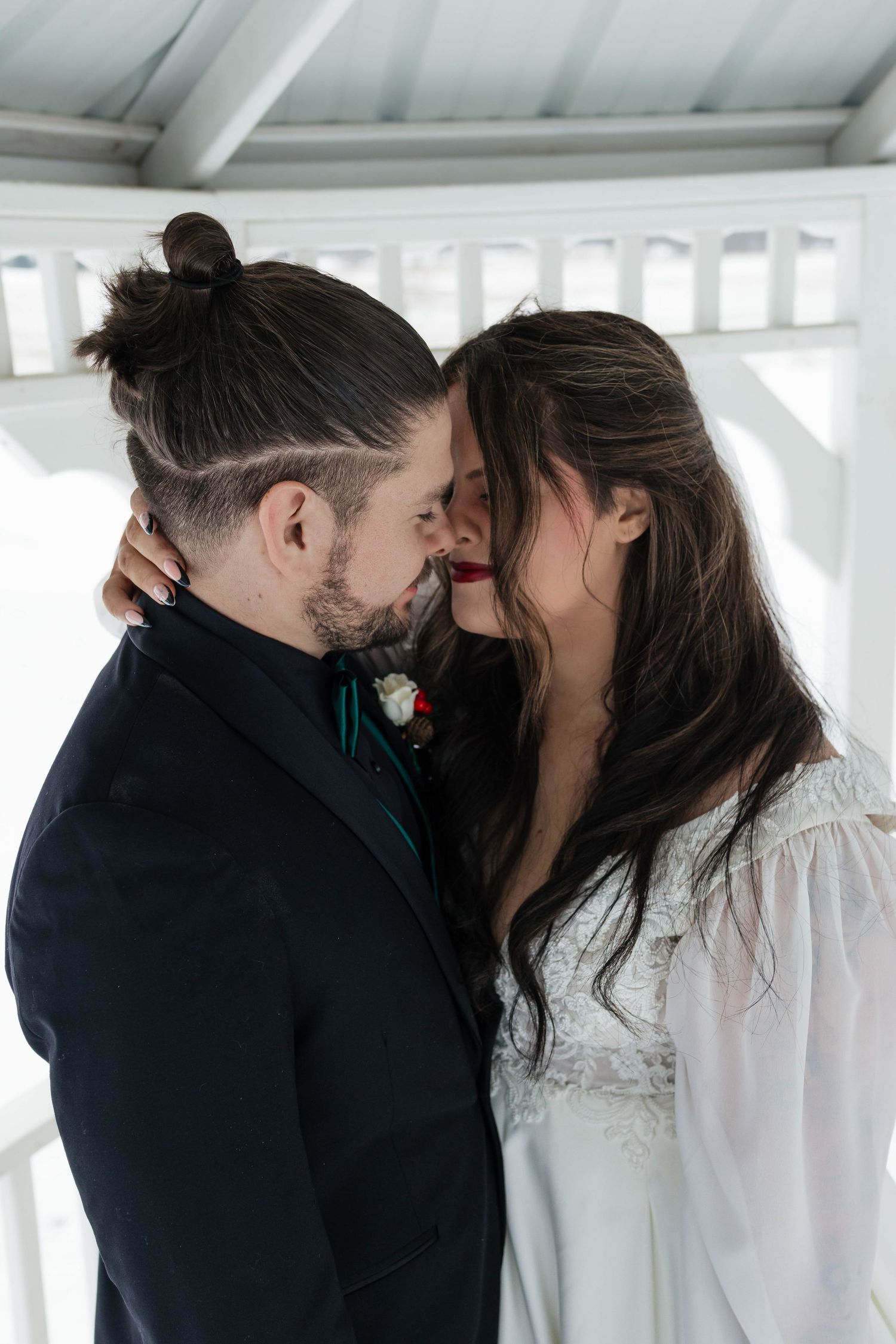 Bride and groom sharing an intimate moment, nearly kissing, in a white outdoor wedding gazebo.