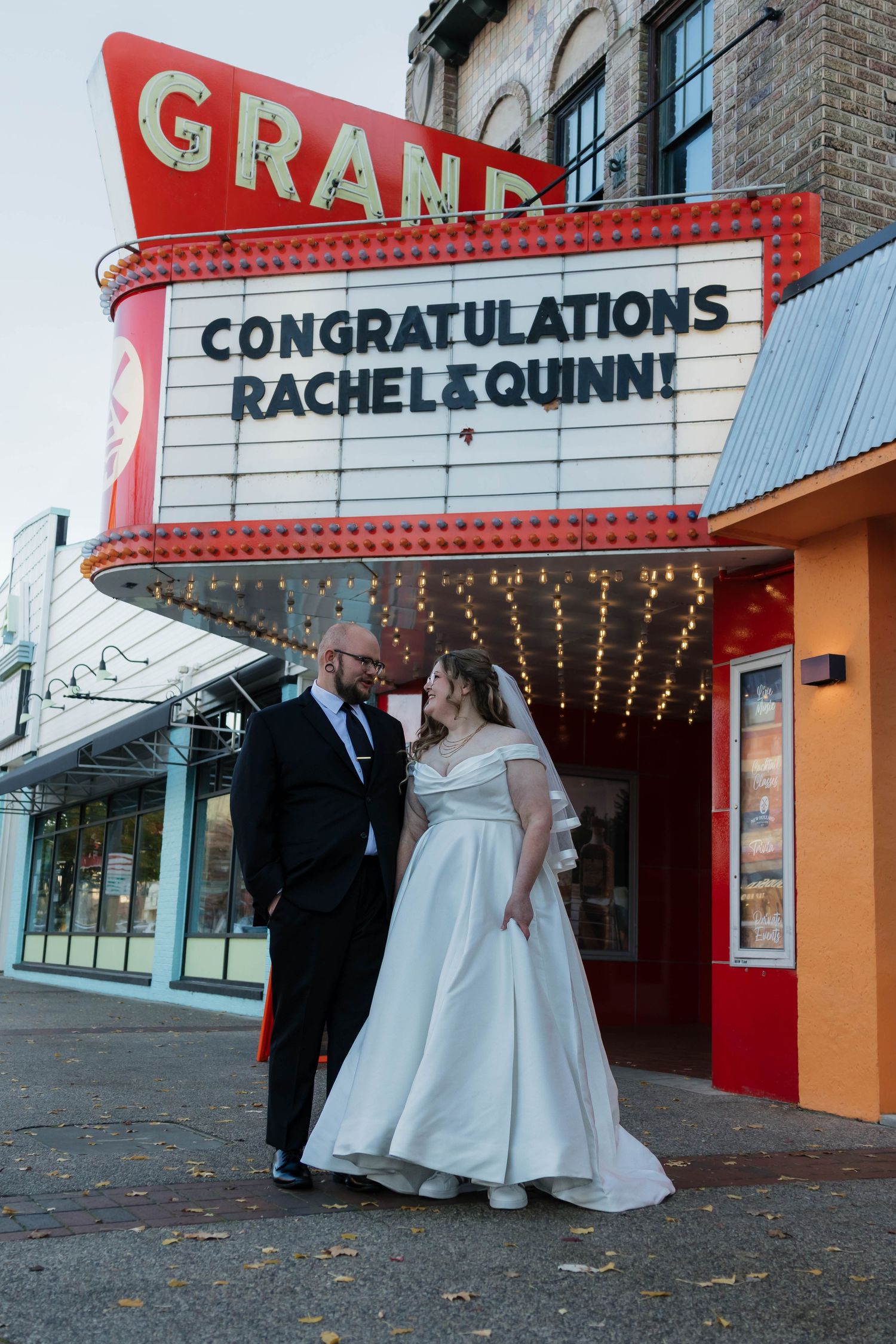 Bride and groom pose under Grand Theatre marquee reading Congratulations Rachel and Quinn at dusk.