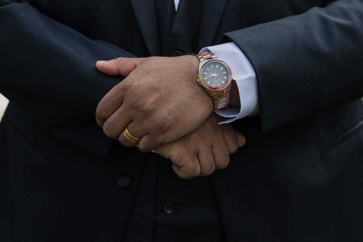 Close-up of groom's hands clasped showing gold wedding band and luxury rose gold watch.