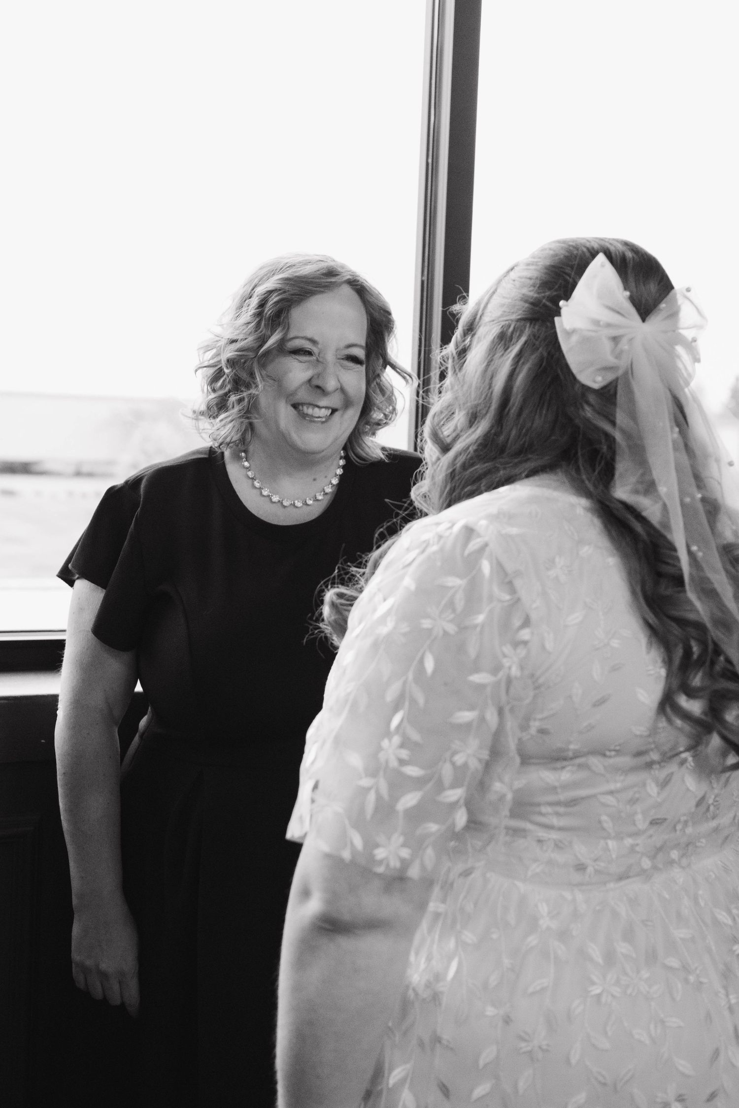 Black and white photo of a woman smiling warmly at the bride before the wedding.