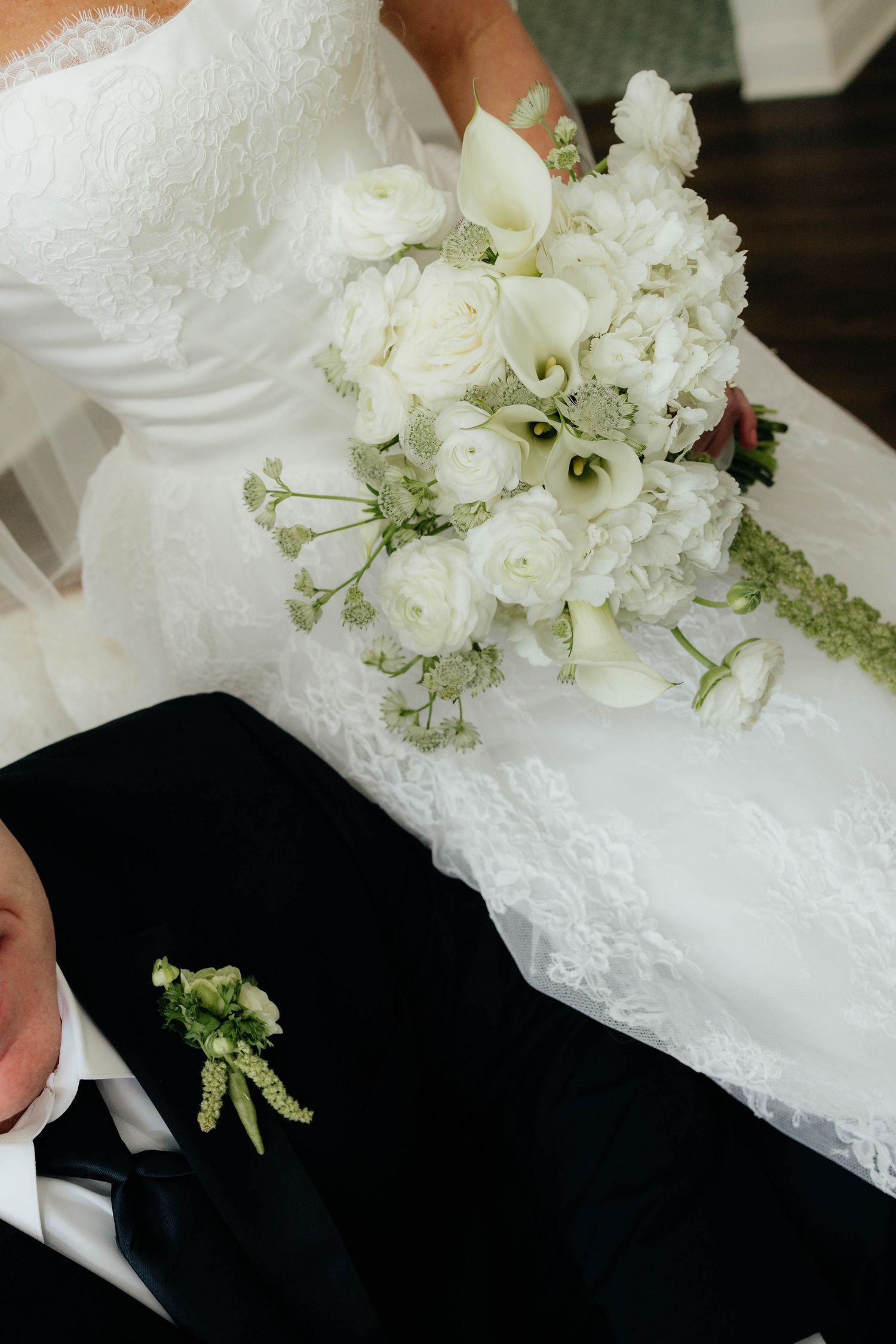 Close-up of bridal bouquet with white roses and calla lilies beside groom's green boutonniere.