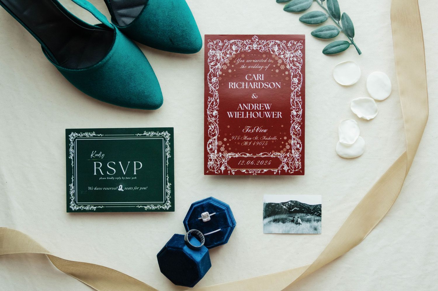 Elegant wedding invitation suite with red and green cards, RSVP, rings in blue velvet box, and teal heels on white background.
