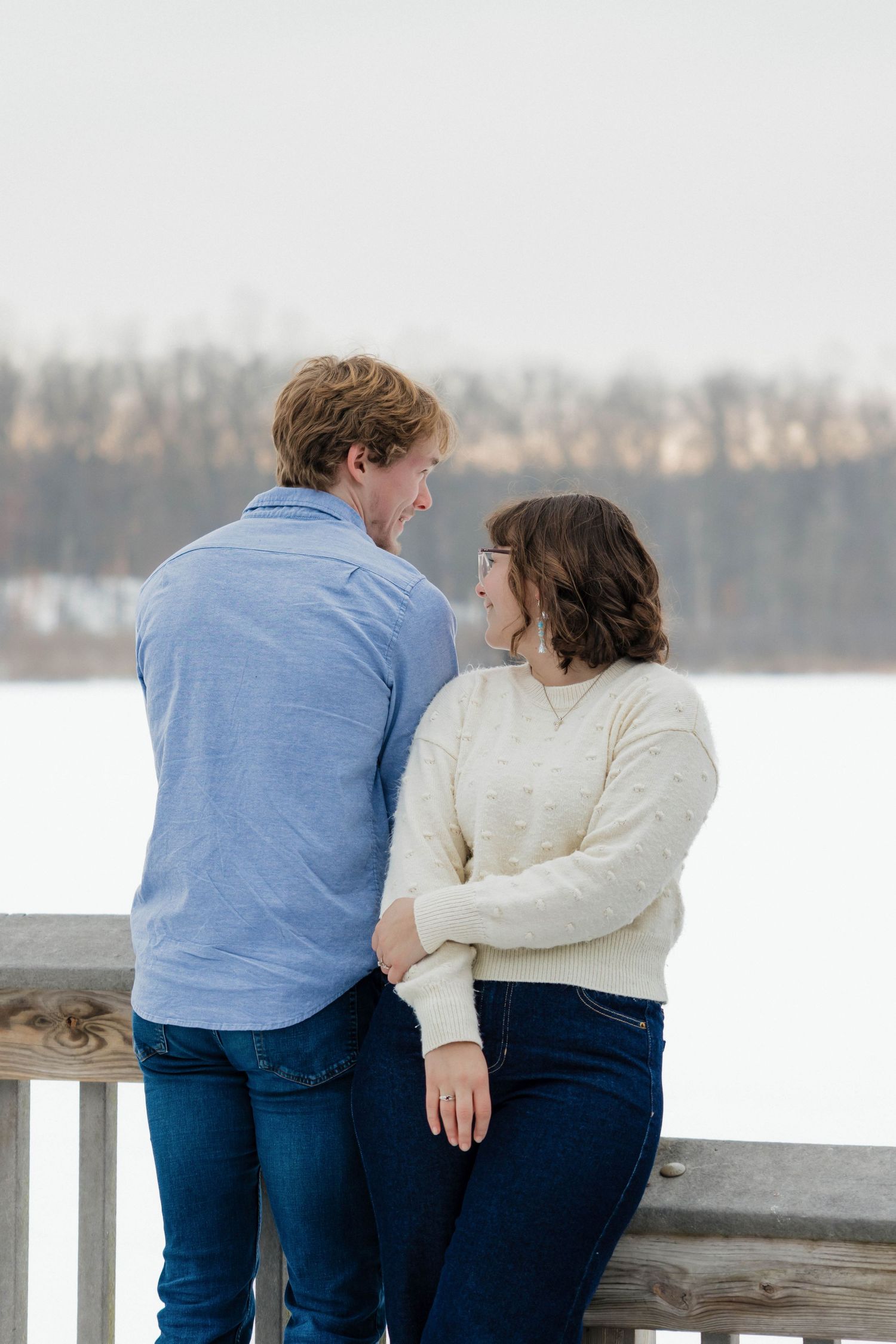 Couple sharing a romantic moment on a snowy wooden deck overlooking a frozen lake in winter.