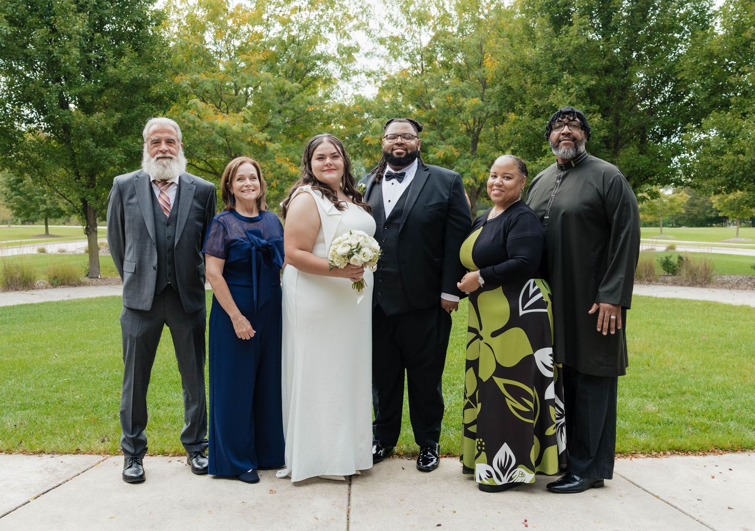 Wedding party of six posing together outdoors on a cloudy autumn day.