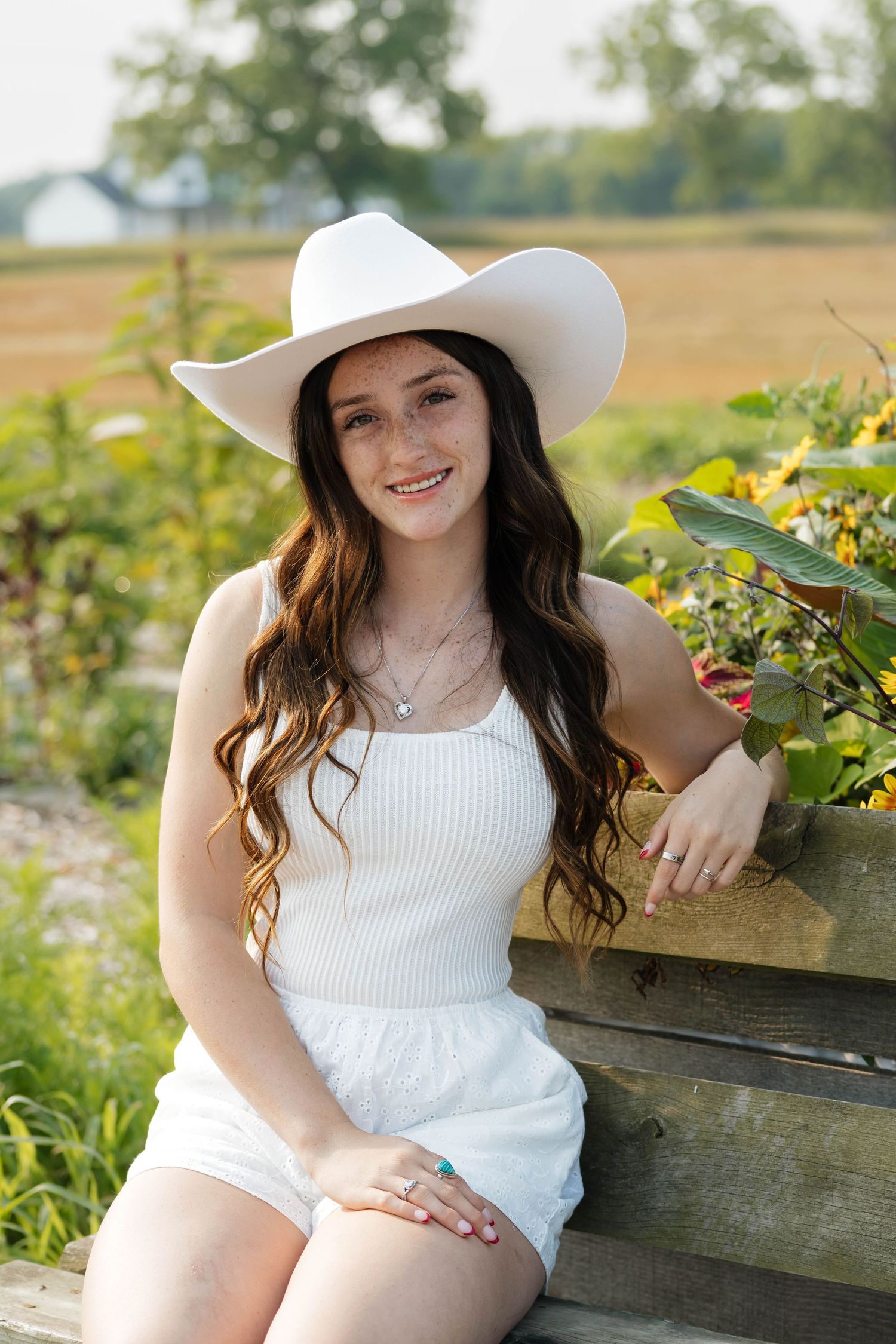 Smiling young woman in white cowboy hat seated by flowers.