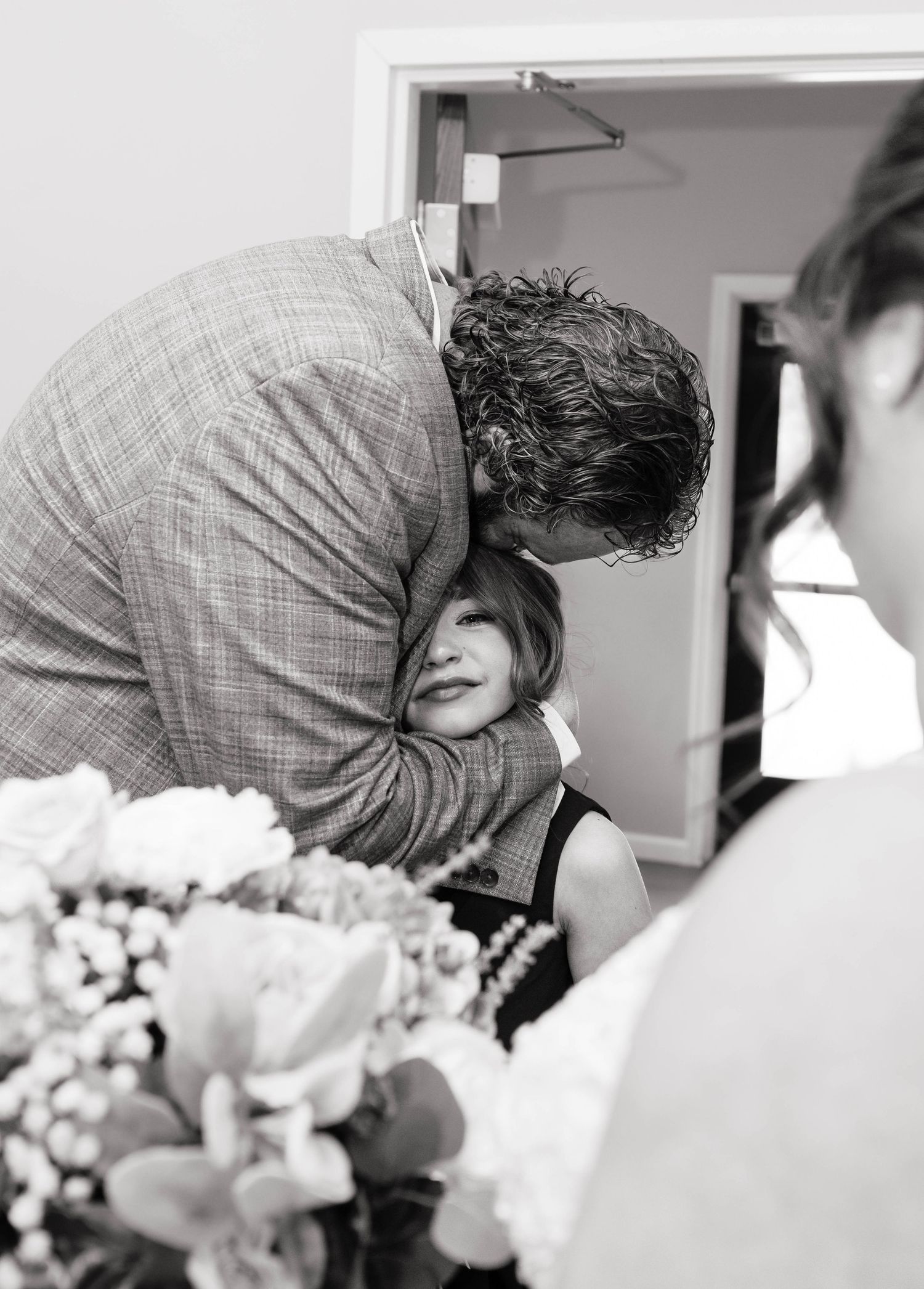 Black and white photo of groom in plaid suit tenderly kissing bride on forehead at wedding.
