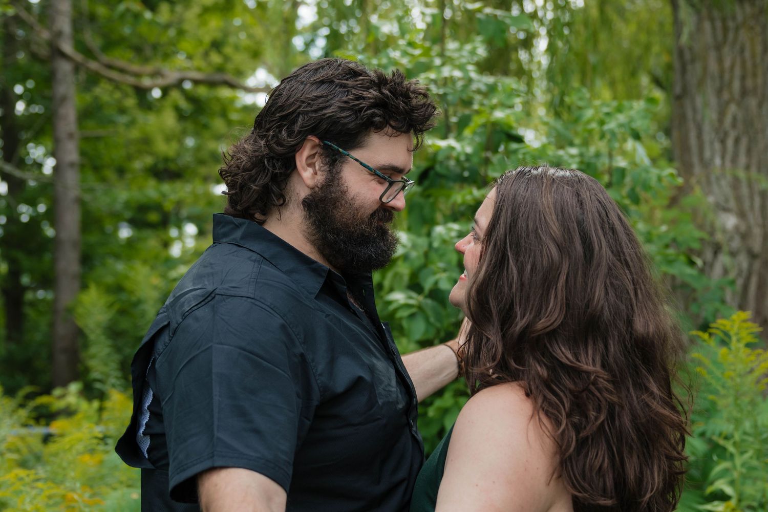 Romantic couple gazing into each others eyes surrounded by green foliage during an outdoor engagement session.