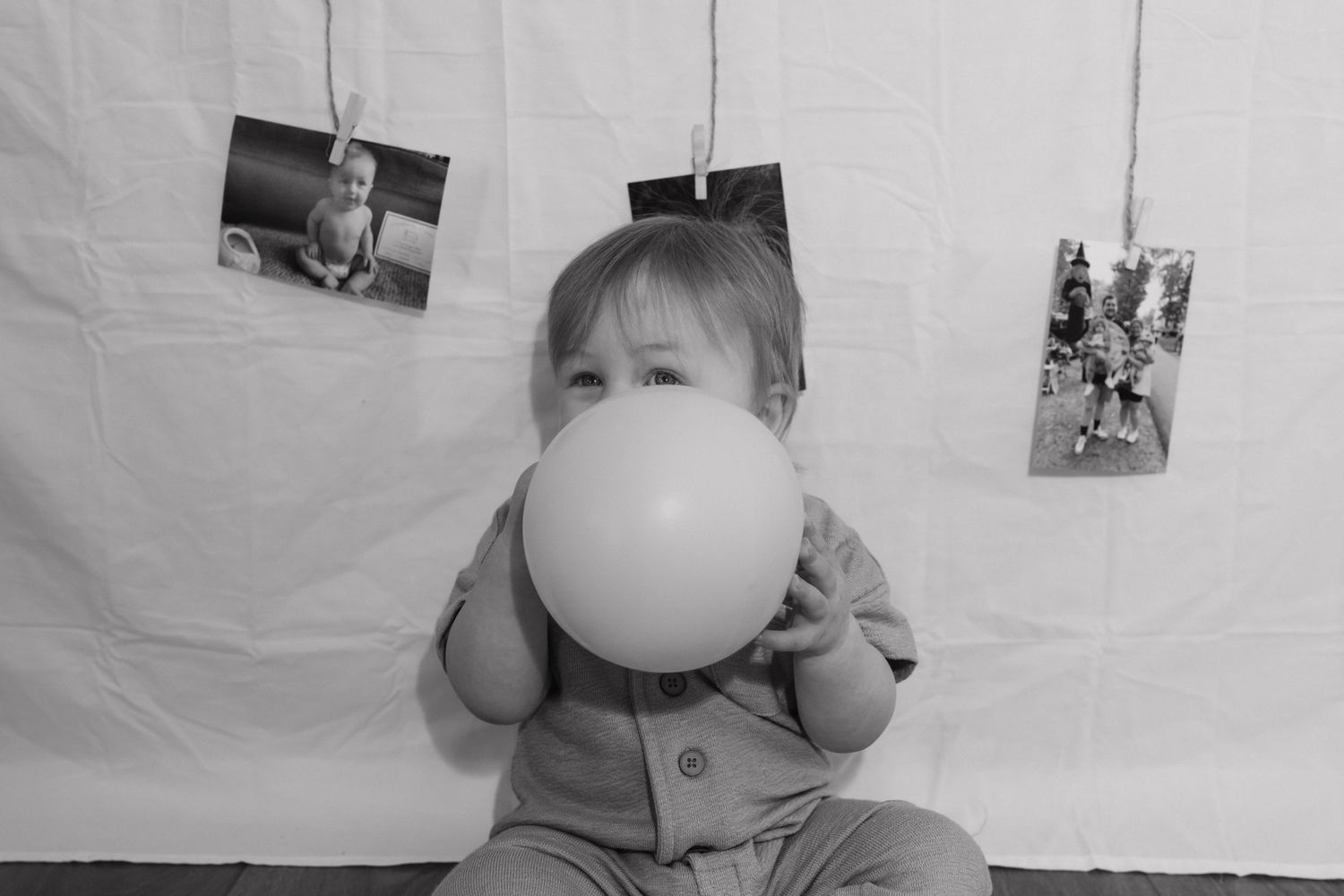 Black and white photo of toddler blowing up balloon at first birthday cake smash session.