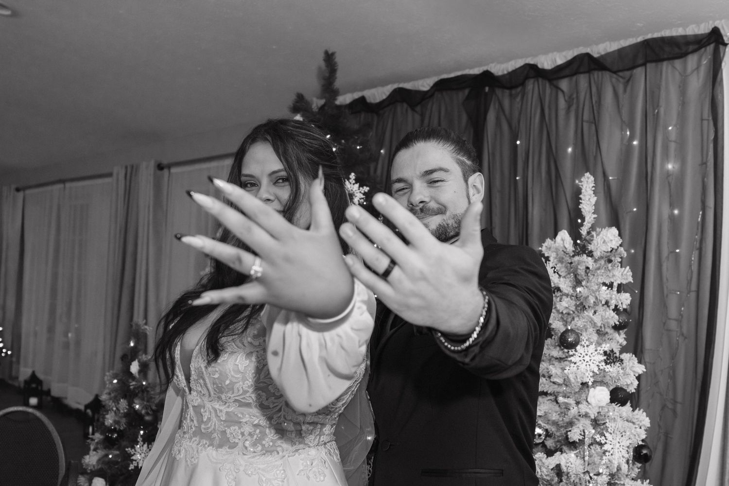 Black and white photo of newlyweds joyfully showing off their wedding rings to the camera.