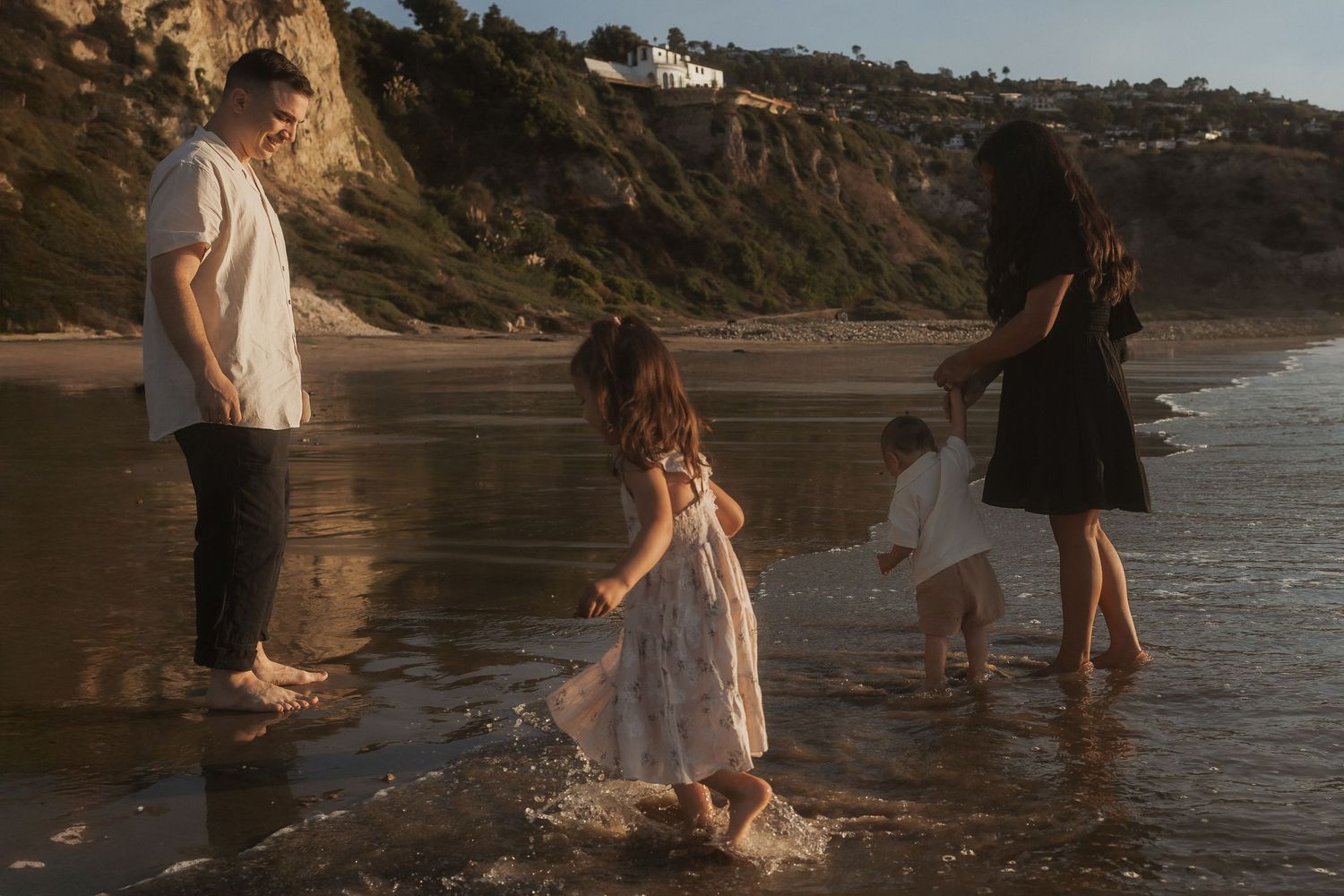 Golden hour beach scene with people enjoying the shoreline and waves along rocky coastal cliffs.