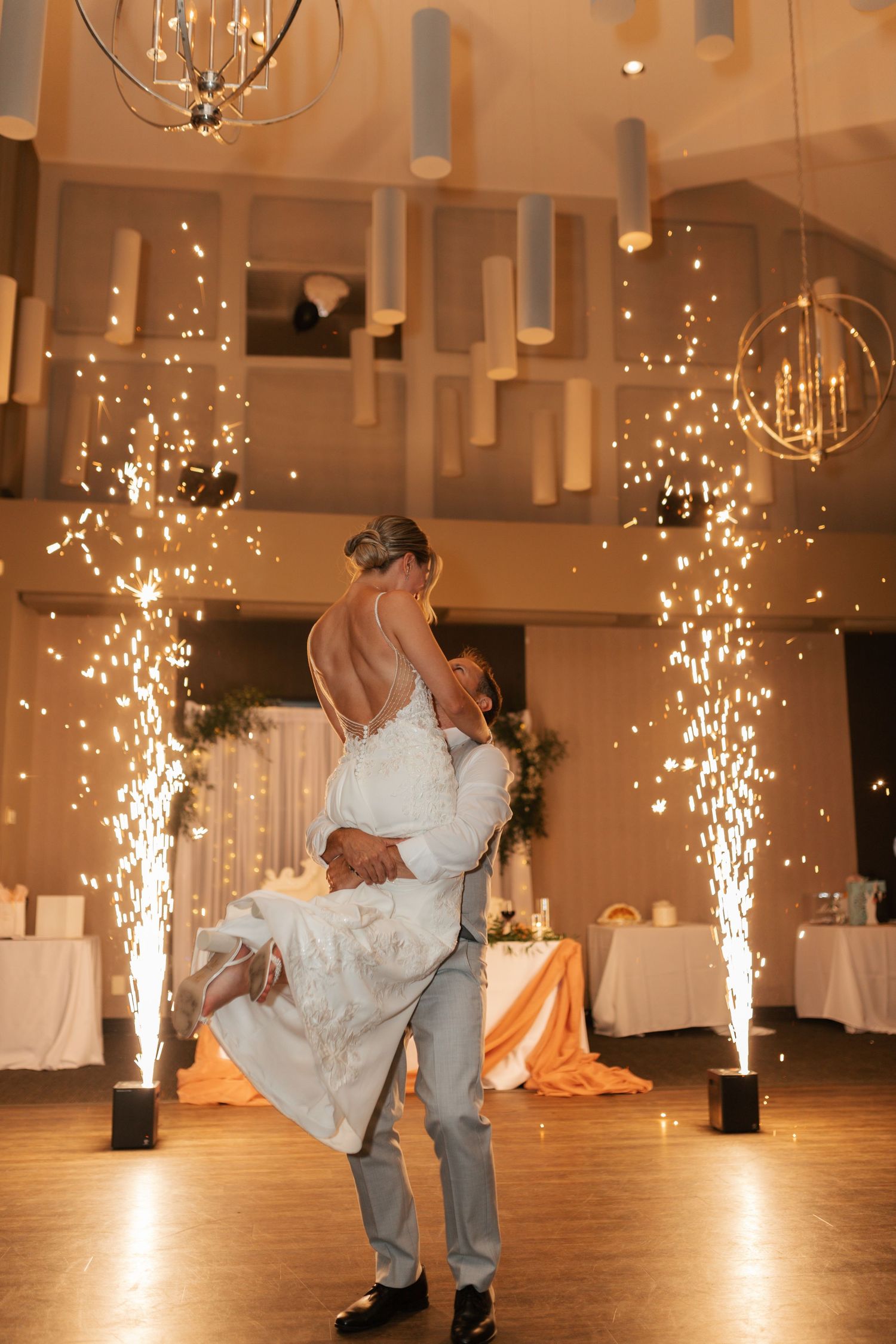 Bride and groom sharing first dance surrounded by sparkling indoor fireworks at elegant wedding reception.
