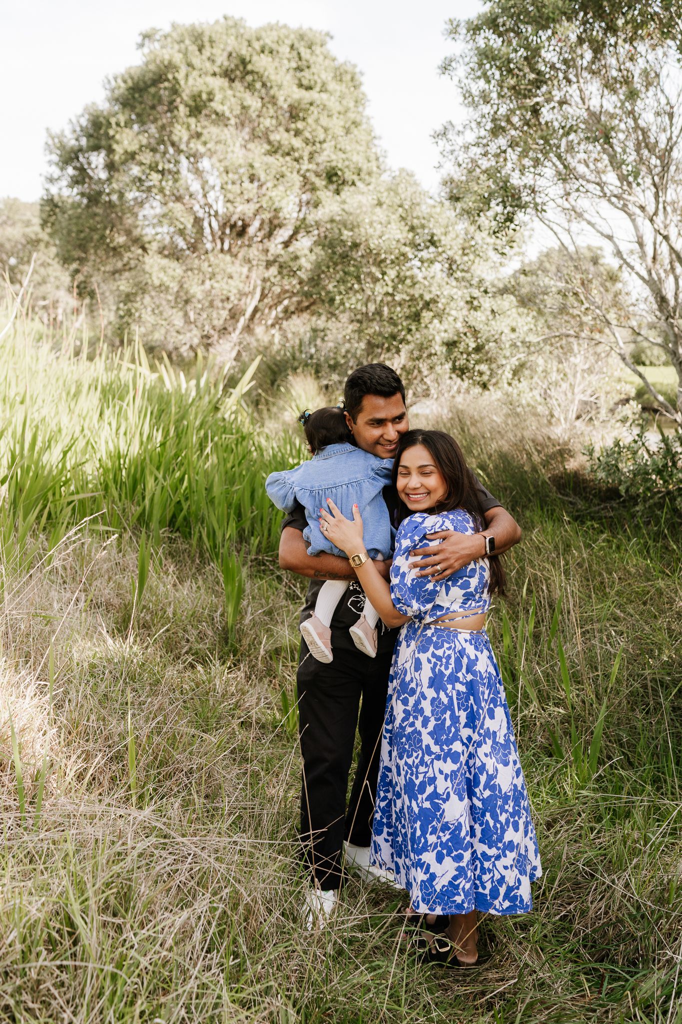 mum, dad and toddler cuddling each other in long grass at an auckland photoshoot