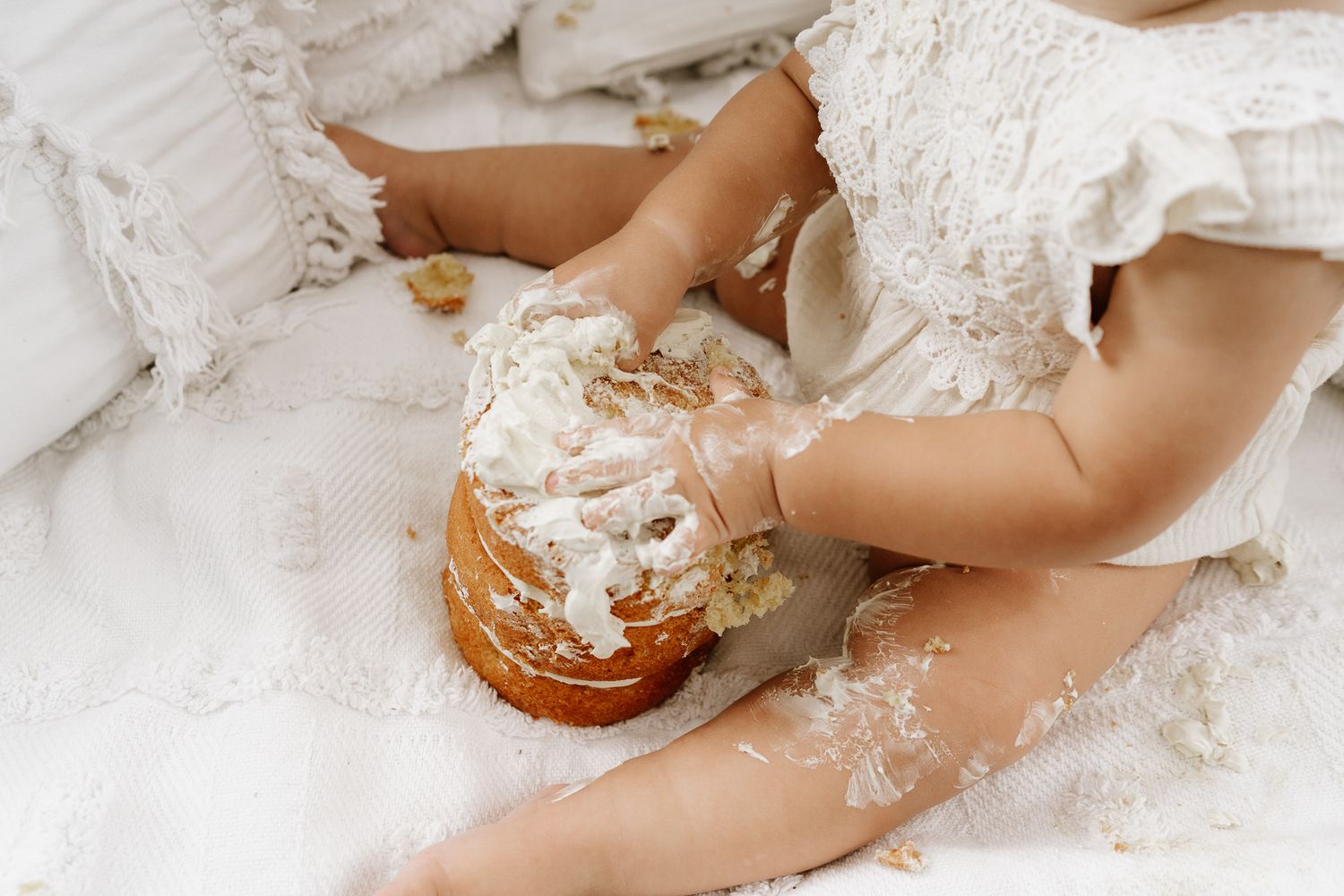 Outdoor cake smash session with a baby seated in front of a teepee, surrounded by long grass. A whimsical, natural setting with playful, mes
