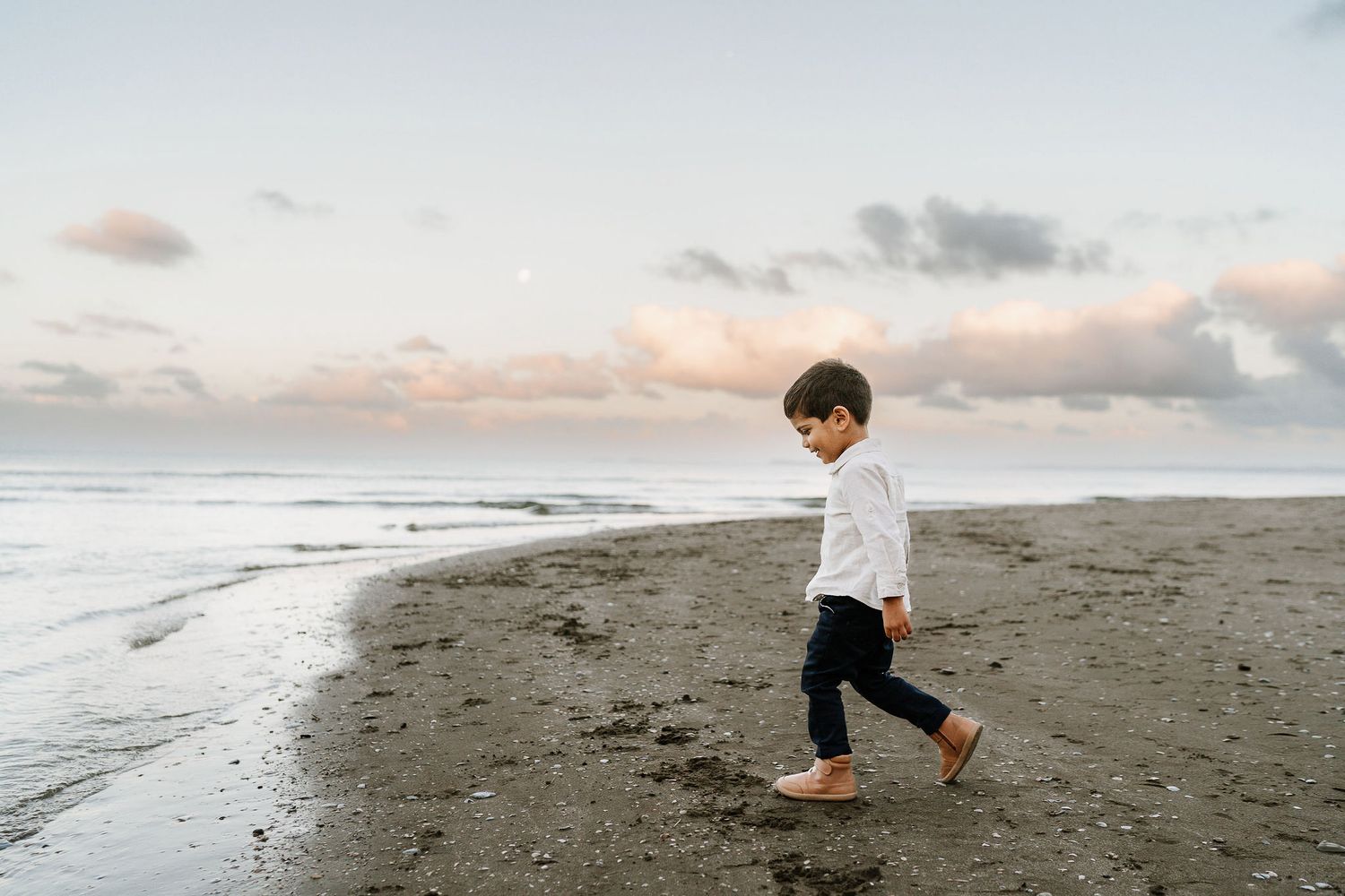 young boy walking along beach at sunset