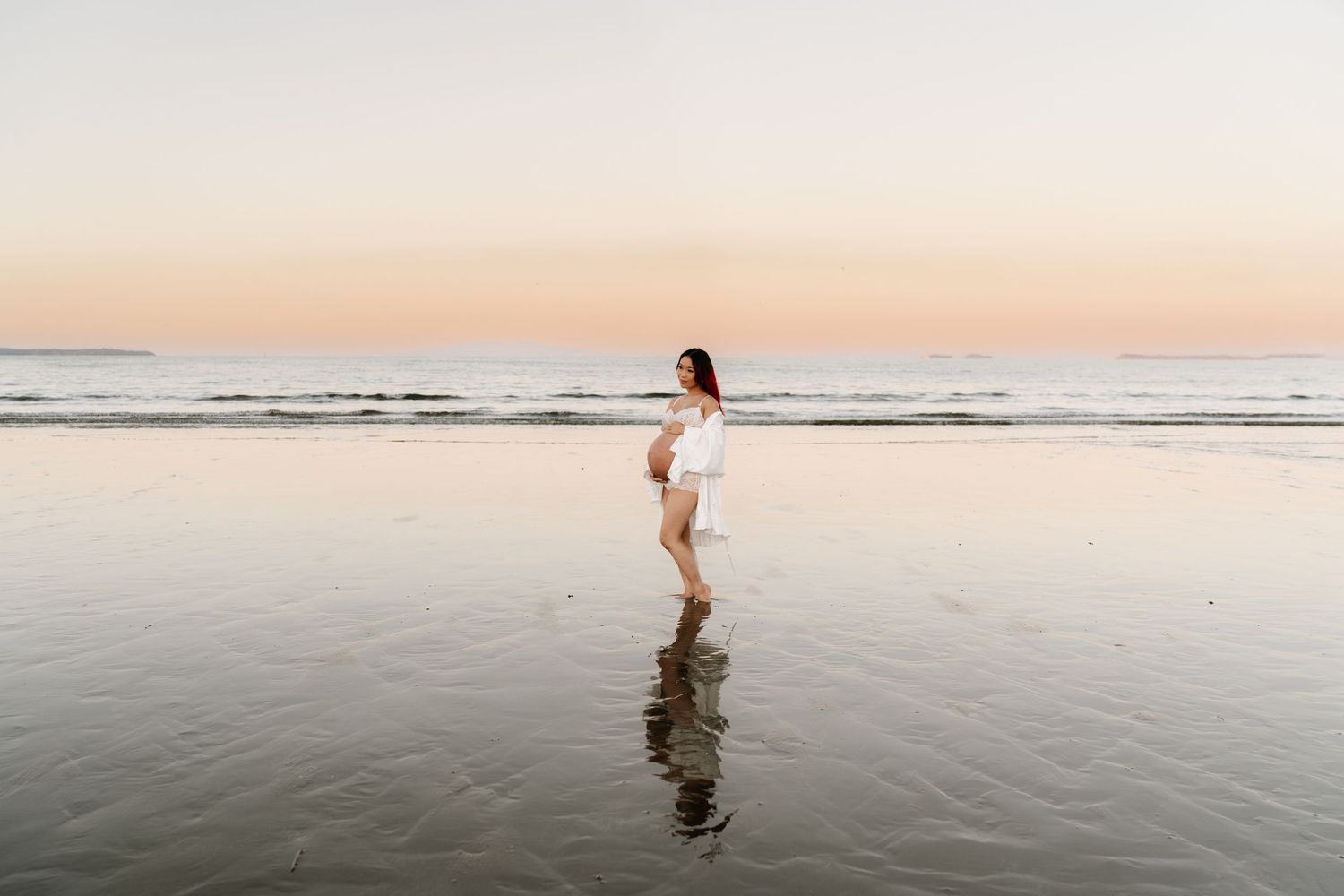 Stunning maternity reflections in the tide at sunset. Bold and modern beach photography by Little Wild Ones, Auckland