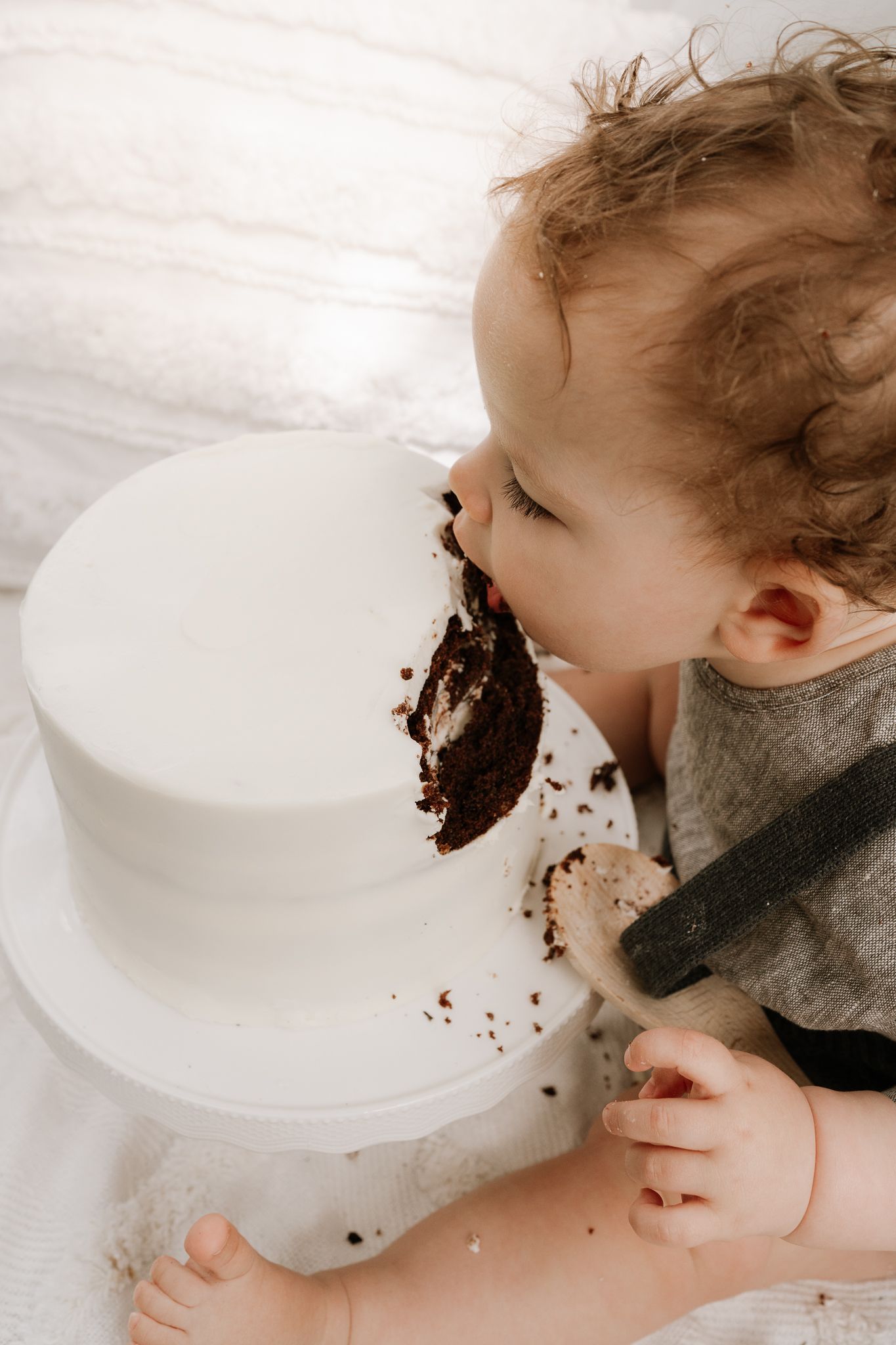 Outdoor cake smash session with a baby seated in front of a teepee, surrounded by long grass. A whimsical, natural setting with playful, mes