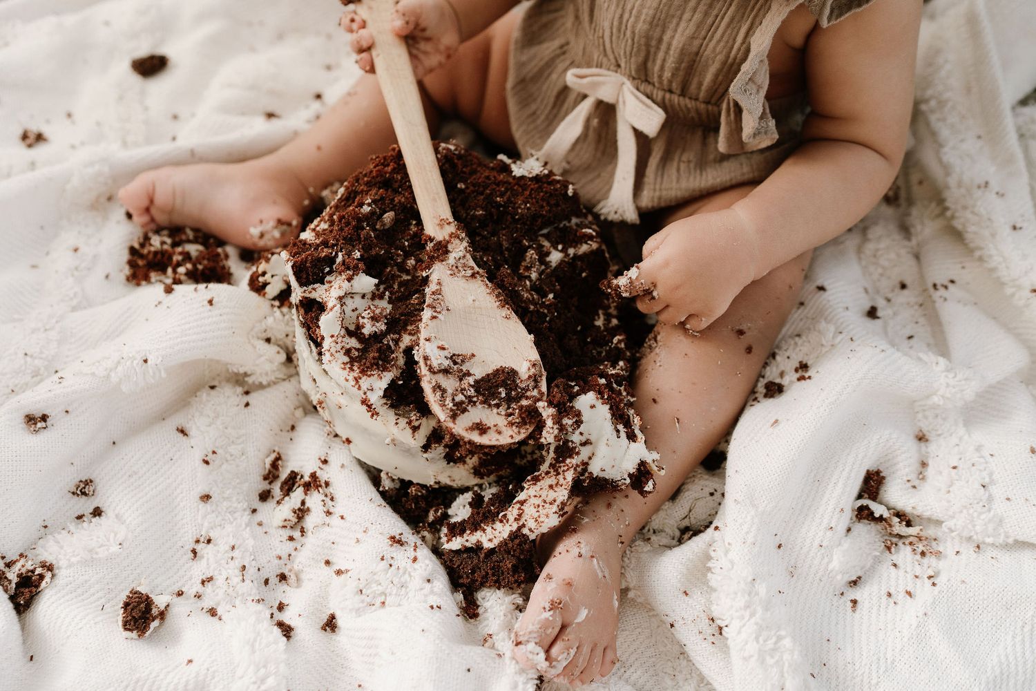 Outdoor cake smash session with a baby seated in front of a teepee, surrounded by long grass. A whimsical, natural setting with playful, mes
