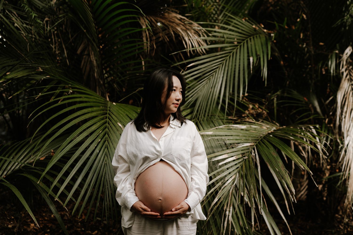 pregnant woman surrounded by native bush, soft light filtering through trees